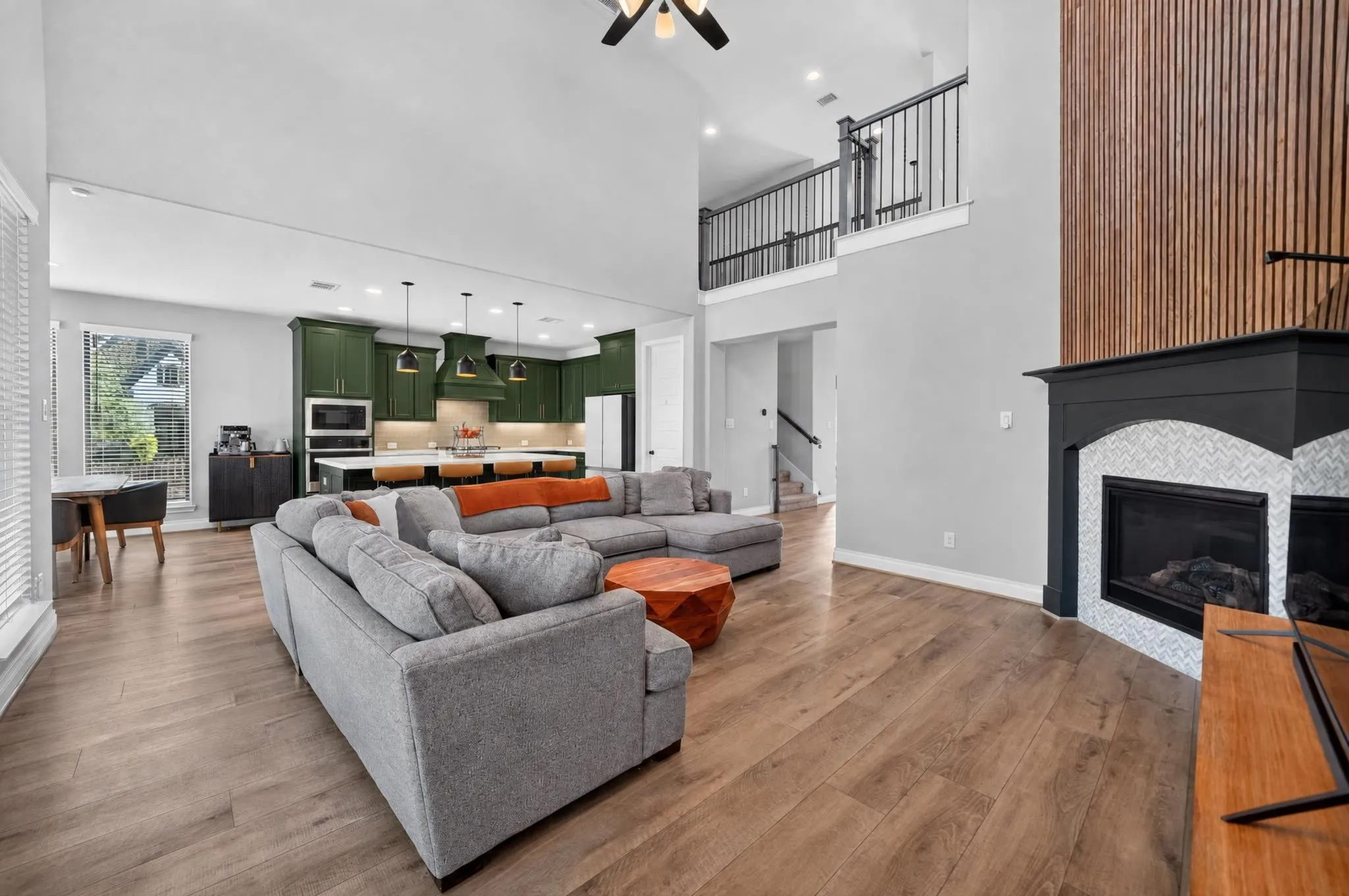 Open-concept living space featuring wood-finish flooring, a two-story ceiling, and a fireplace with a tiled surround