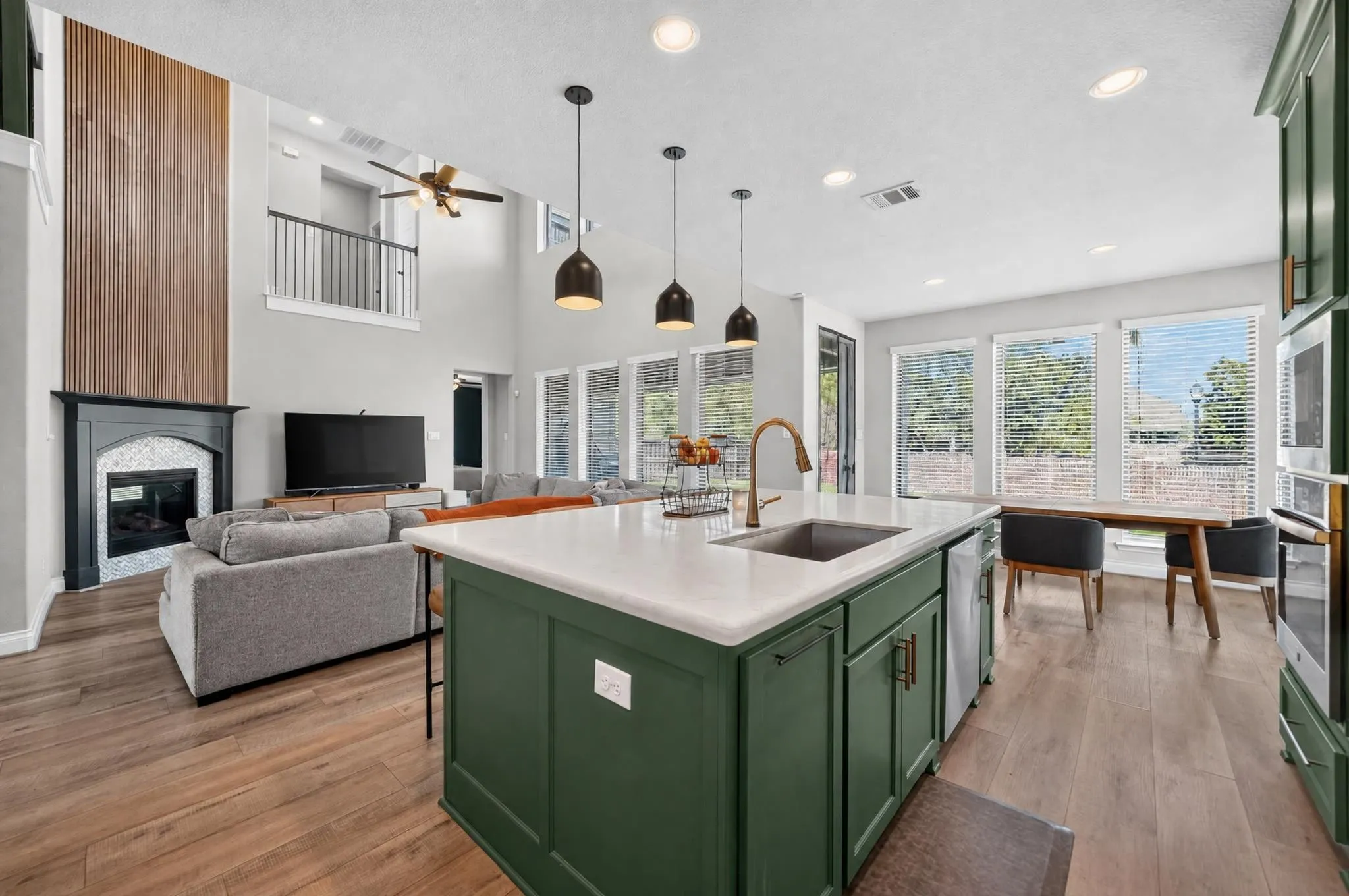 Open-concept living space featuring a two-story fireplace with a decorative wood accent wall, wood-finish flooring, and a kitchen island with a built-in sink and pendant lighting