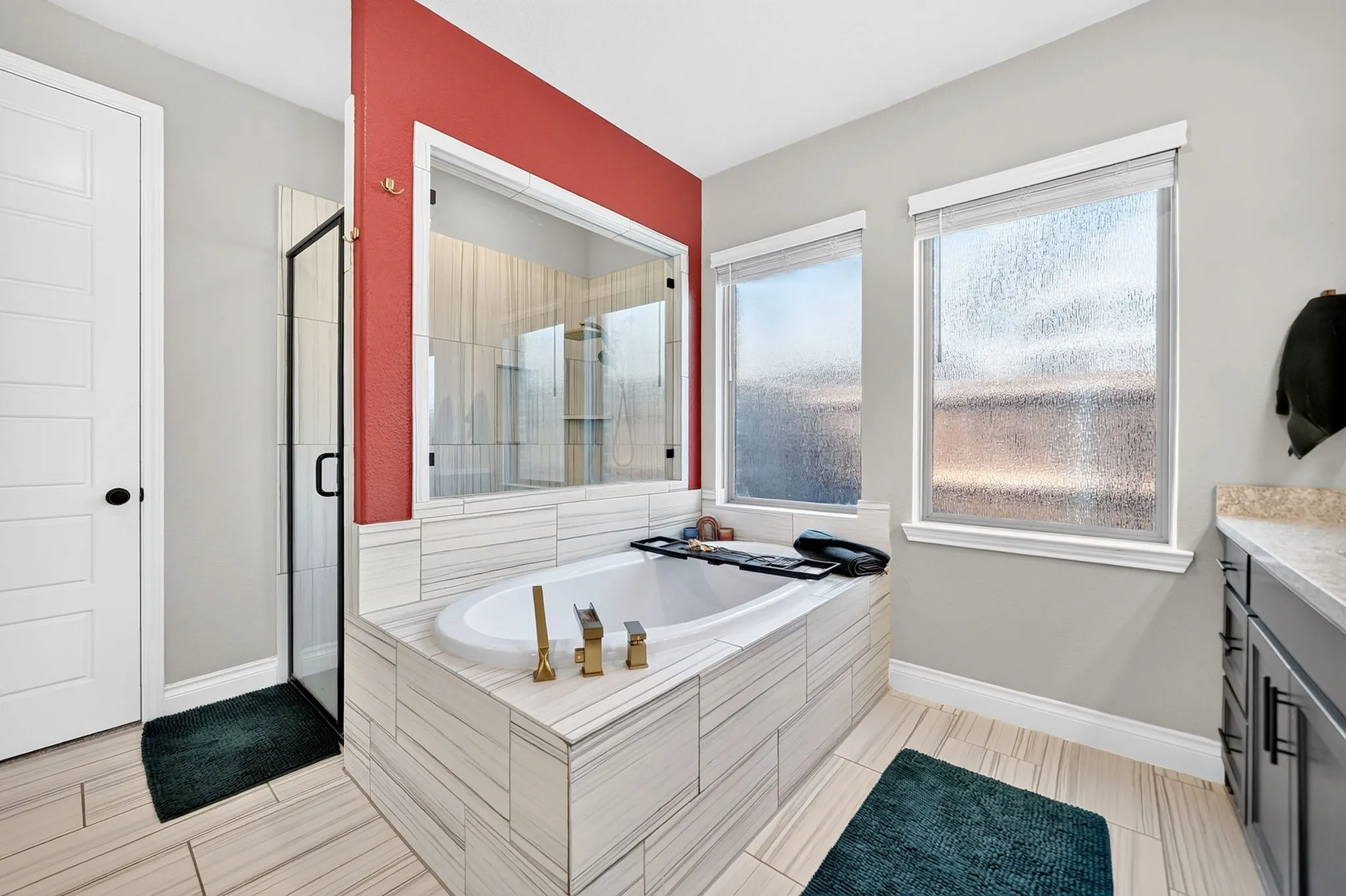 Soaking tub with brass-finish fixtures, tile surround, and an adjacent glass-enclosed shower