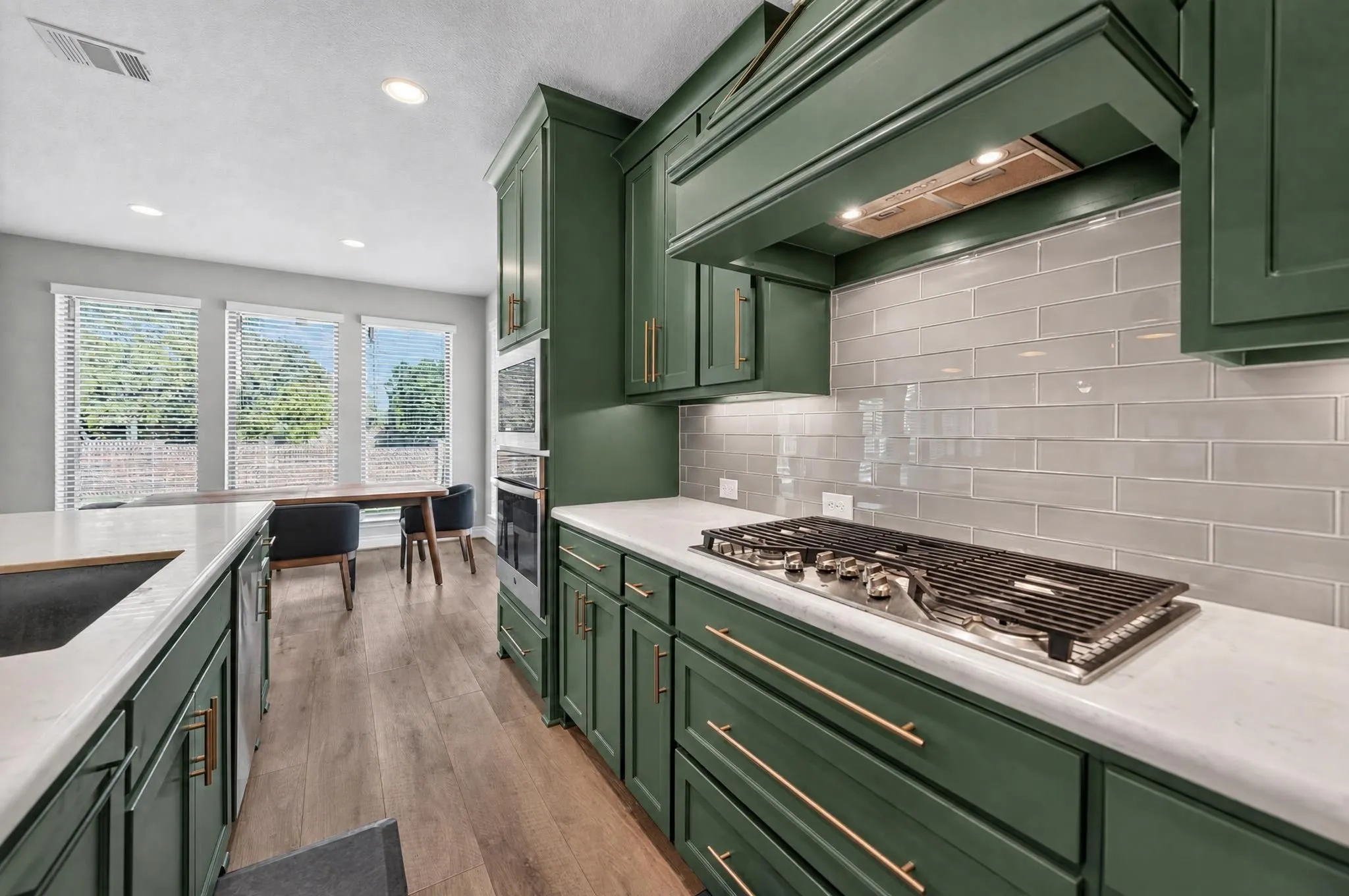 Green cabinetry with brass hardware, a gas cooktop, light-colored subway tile backsplash, white countertops, and wood-finish flooring