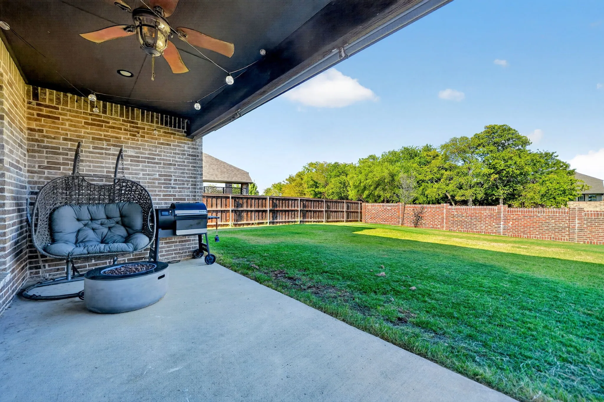 Covered patio with brick wall, ceiling fan, and string lighting