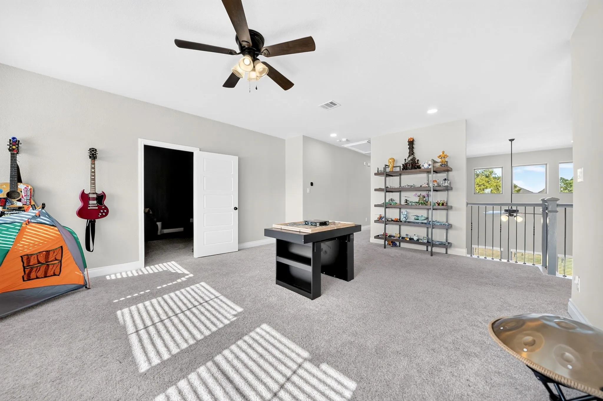 Carpeted floor, neutral wall paint, ceiling fan with integrated lighting, white paneled door, and wrought iron railing