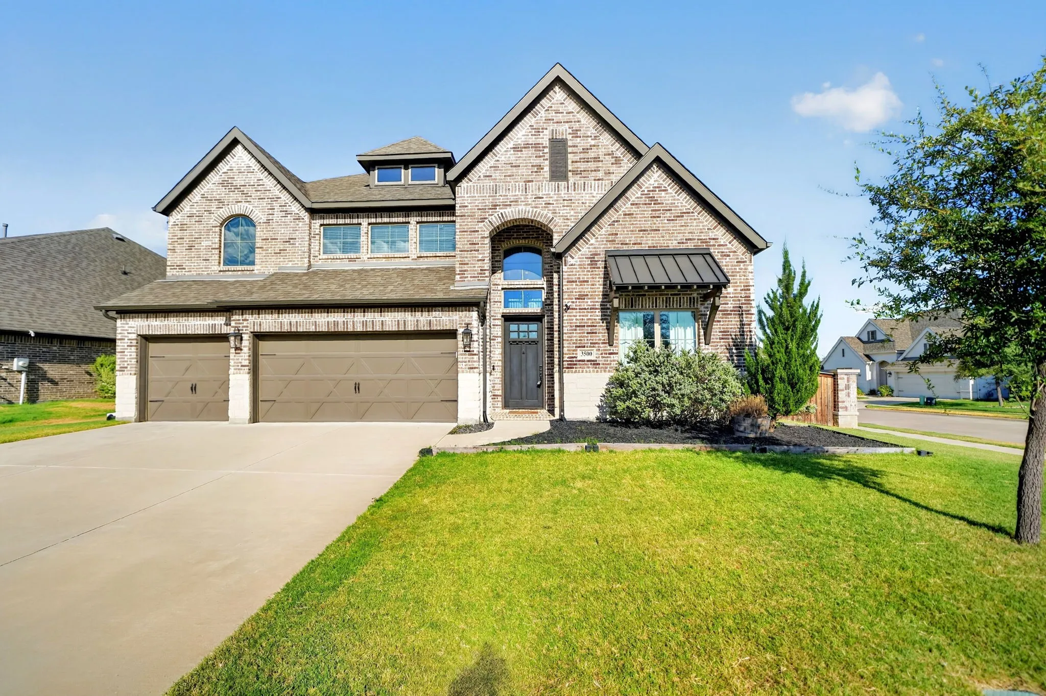 Brick facade with stone accents, arched entryway, dormer window, two-car garage, and landscaped front yard