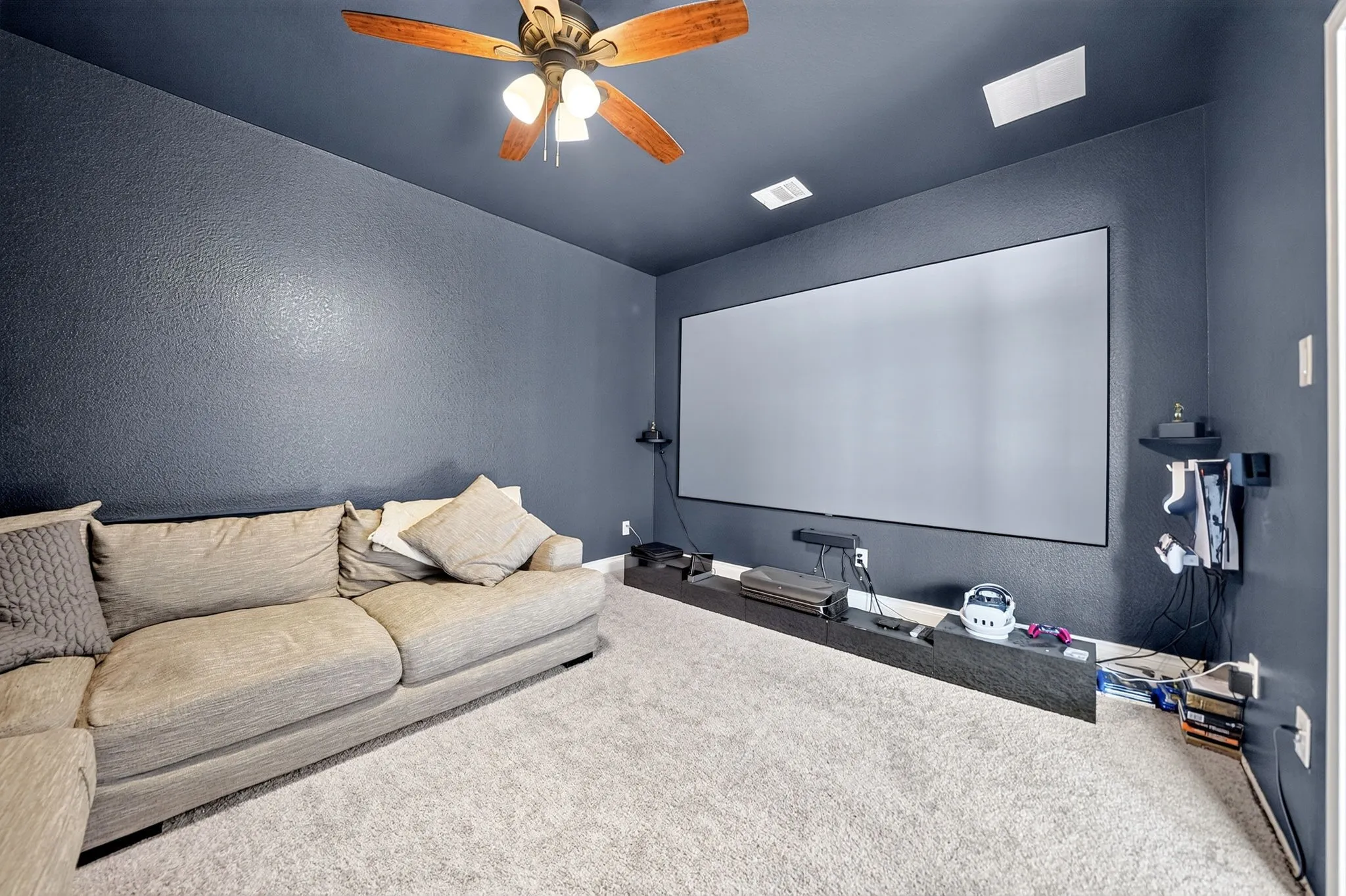 Wall-mounted projection screen with dedicated media display shelf, textured wall finish, wood-blade ceiling fan, and recessed lighting