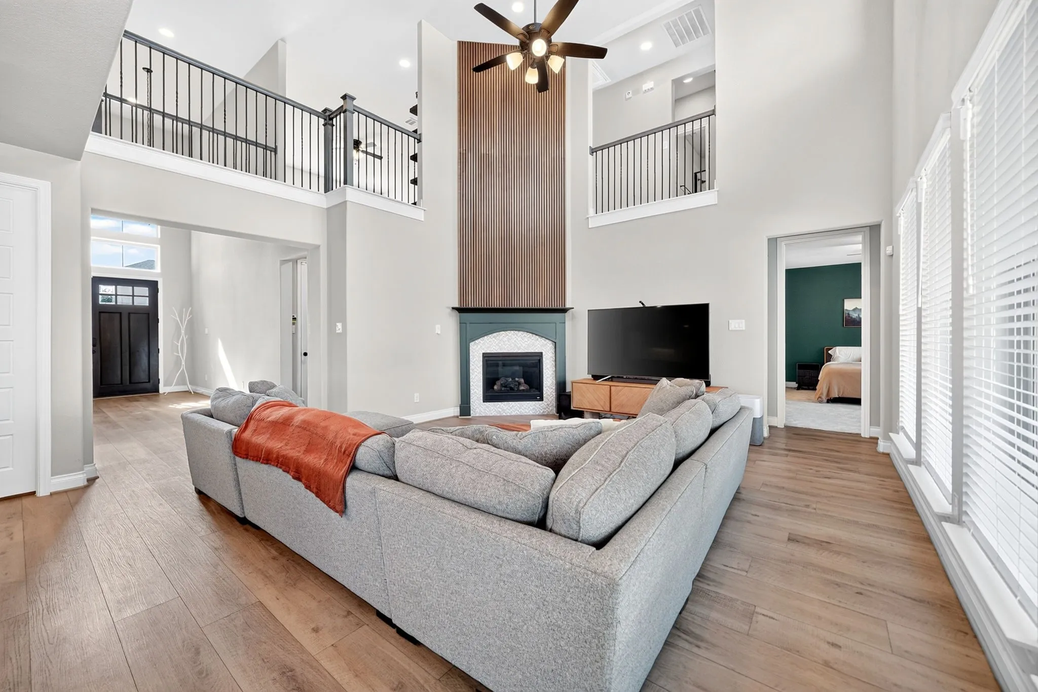 Two-story living area with high ceilings, wood-finish flooring, a fireplace with a wood-paneled accent wall, and an open balcony overlooking the space