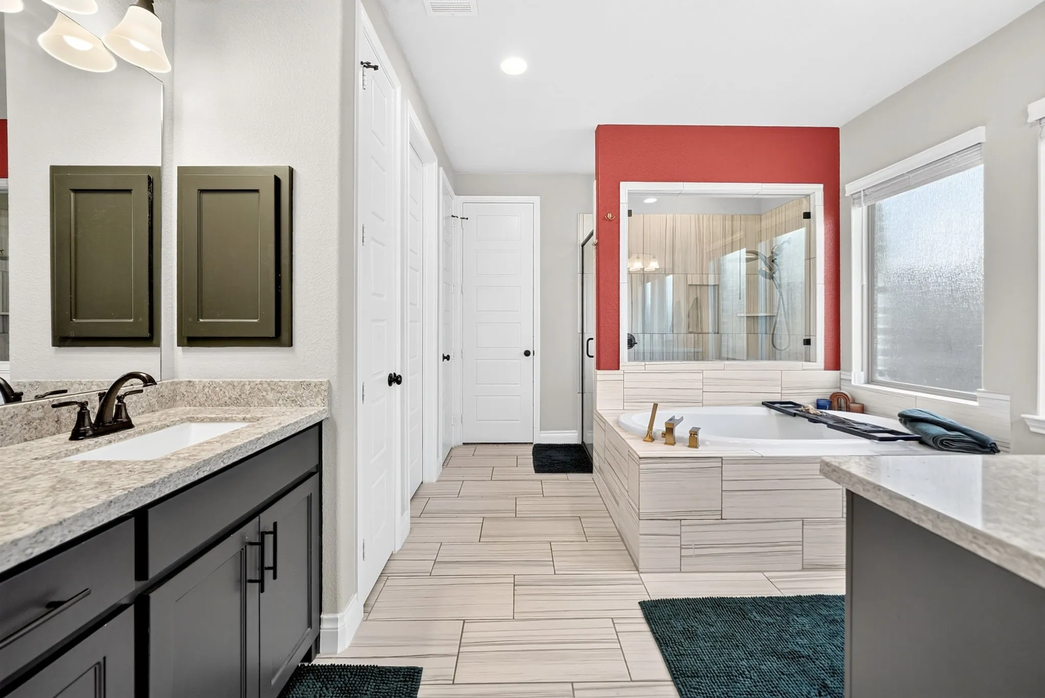 Dual vanity with dark cabinetry and light-toned countertop, large soaking tub with tiled surround, glass-enclosed shower, and wood-finish flooring