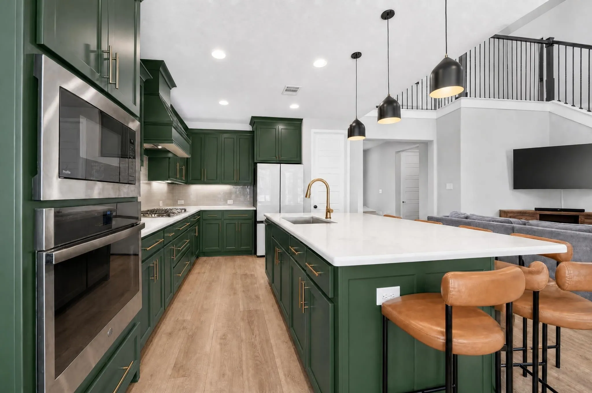 Kitchen featuring rich green cabinetry, stainless steel appliances, a center island with a sink, and wood-finish flooring