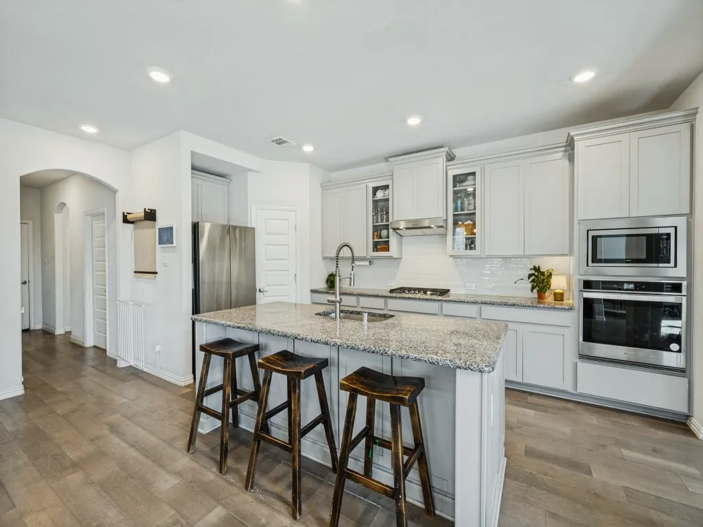 Kitchen featuring a large island with granite counters, stainless steel appliances, white cabinetry, and wood-finish flooring