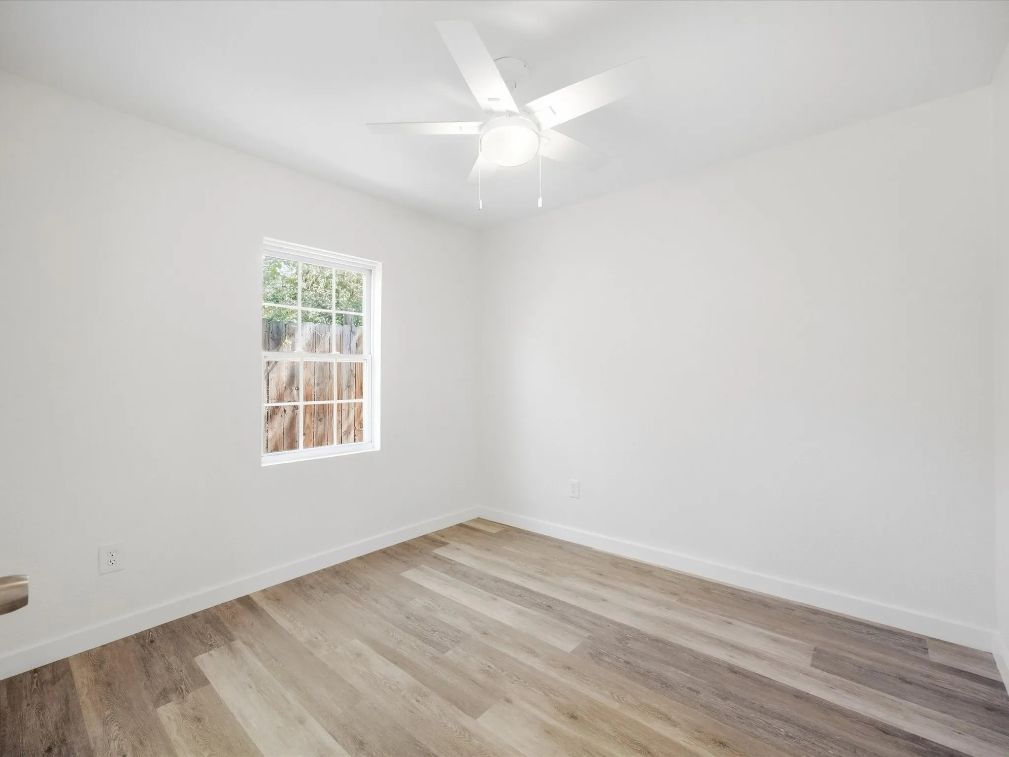 White interior walls, wood-finish flooring, white ceiling fan, and a multi-pane window