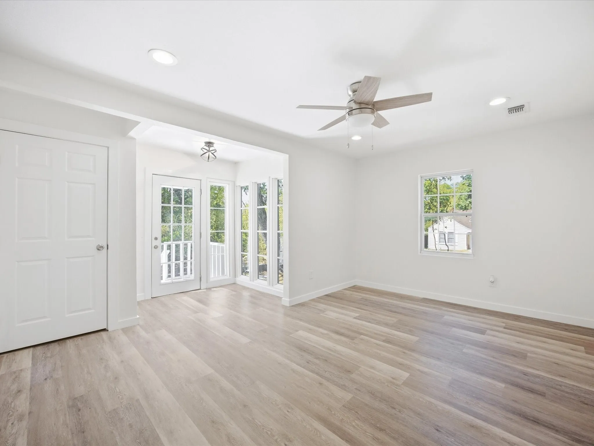 Wood-finish flooring, recessed lighting, ceiling fan, white paneled doors, and French doors with transom windows