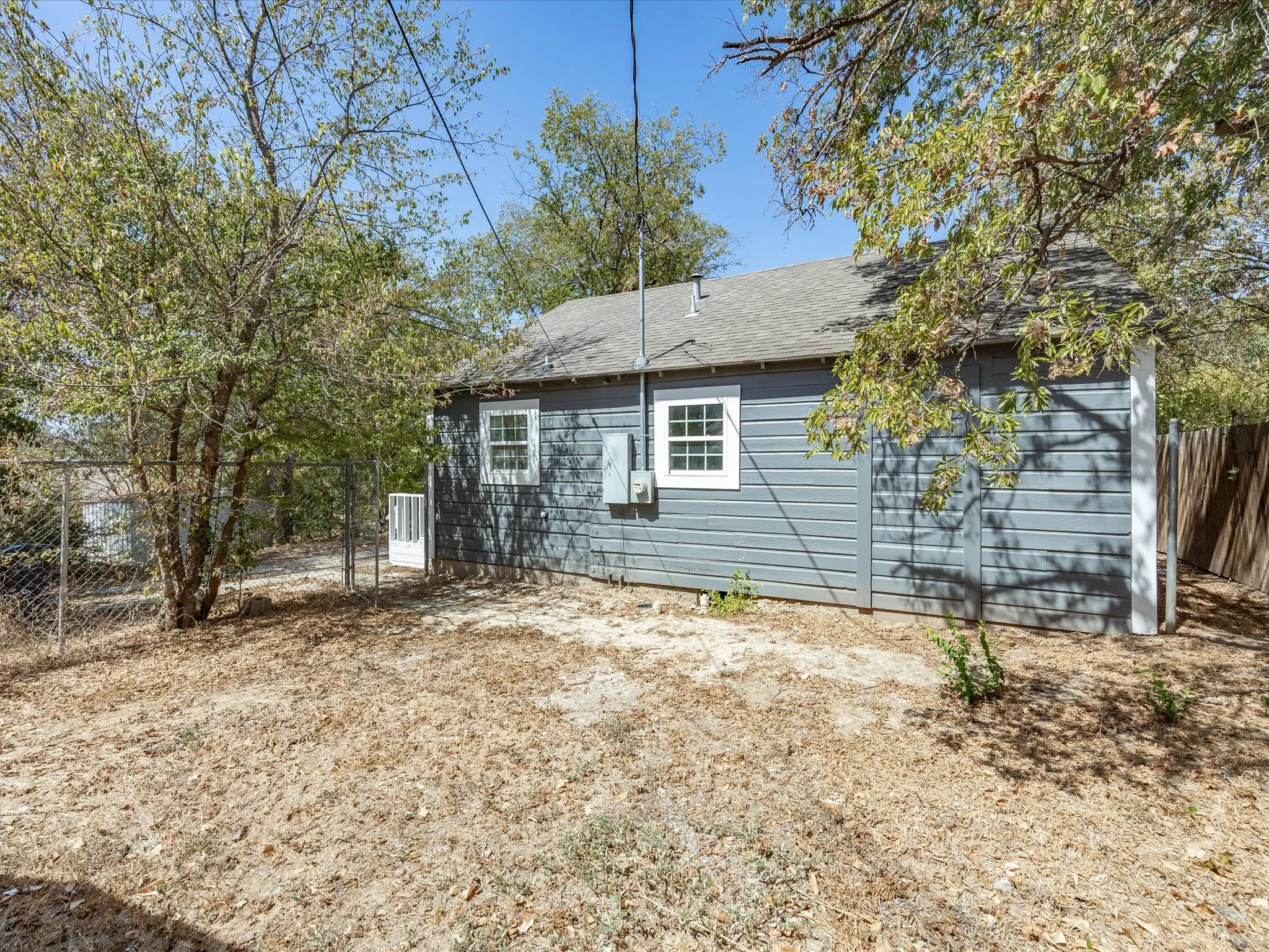 Exterior siding with white-framed windows, shingled roof, and chain-link fencing