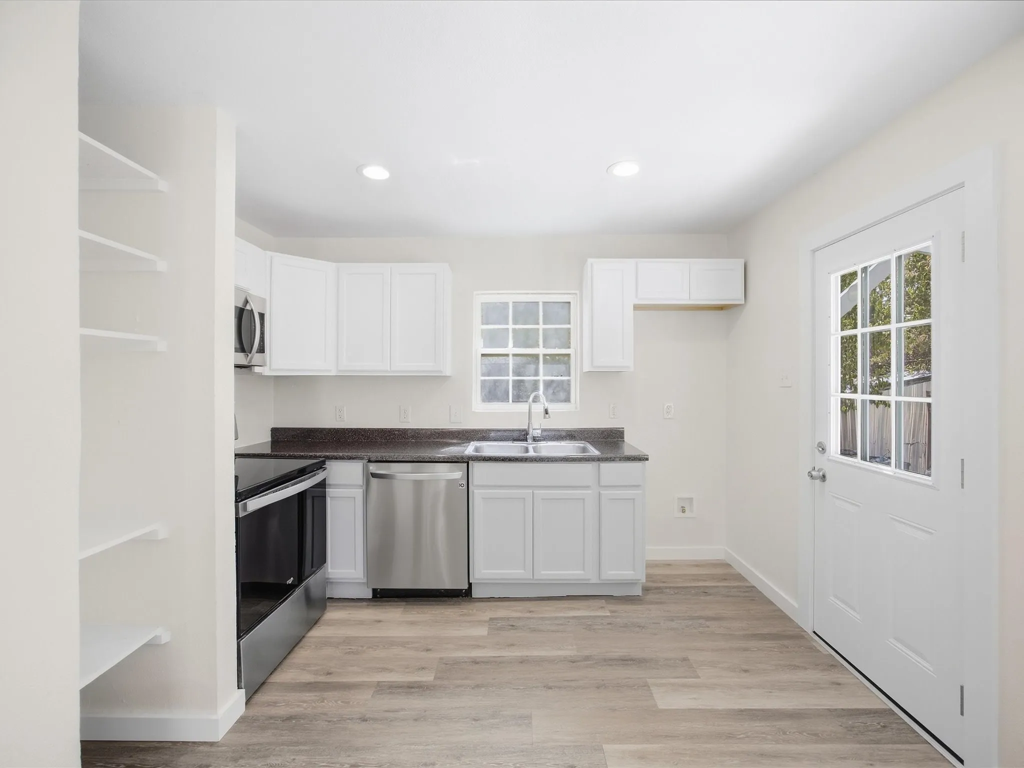Kitchen featuring white cabinetry, dark countertops, stainless steel appliances, wood-finish flooring, and a glass-paned door