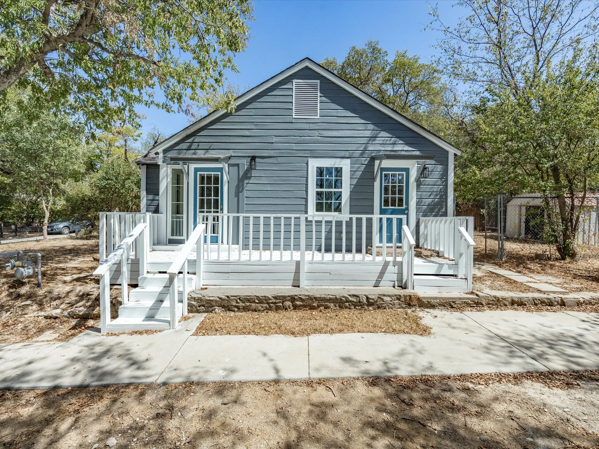 Blue siding exterior with white trim, a covered front porch with white railing, and a gabled roofline