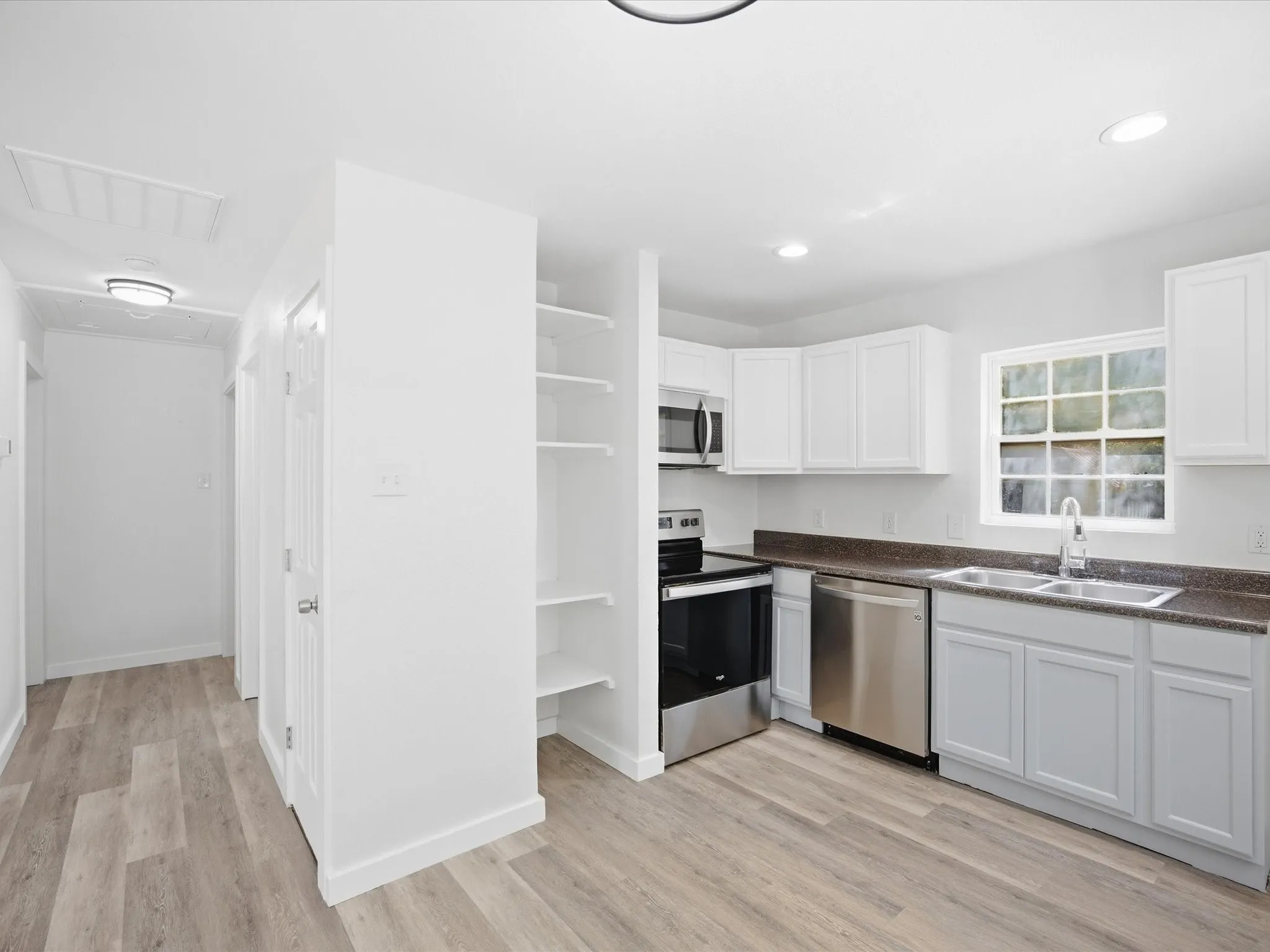 Kitchen featuring white cabinetry, dark countertops, stainless steel appliances, and wood-finish flooring