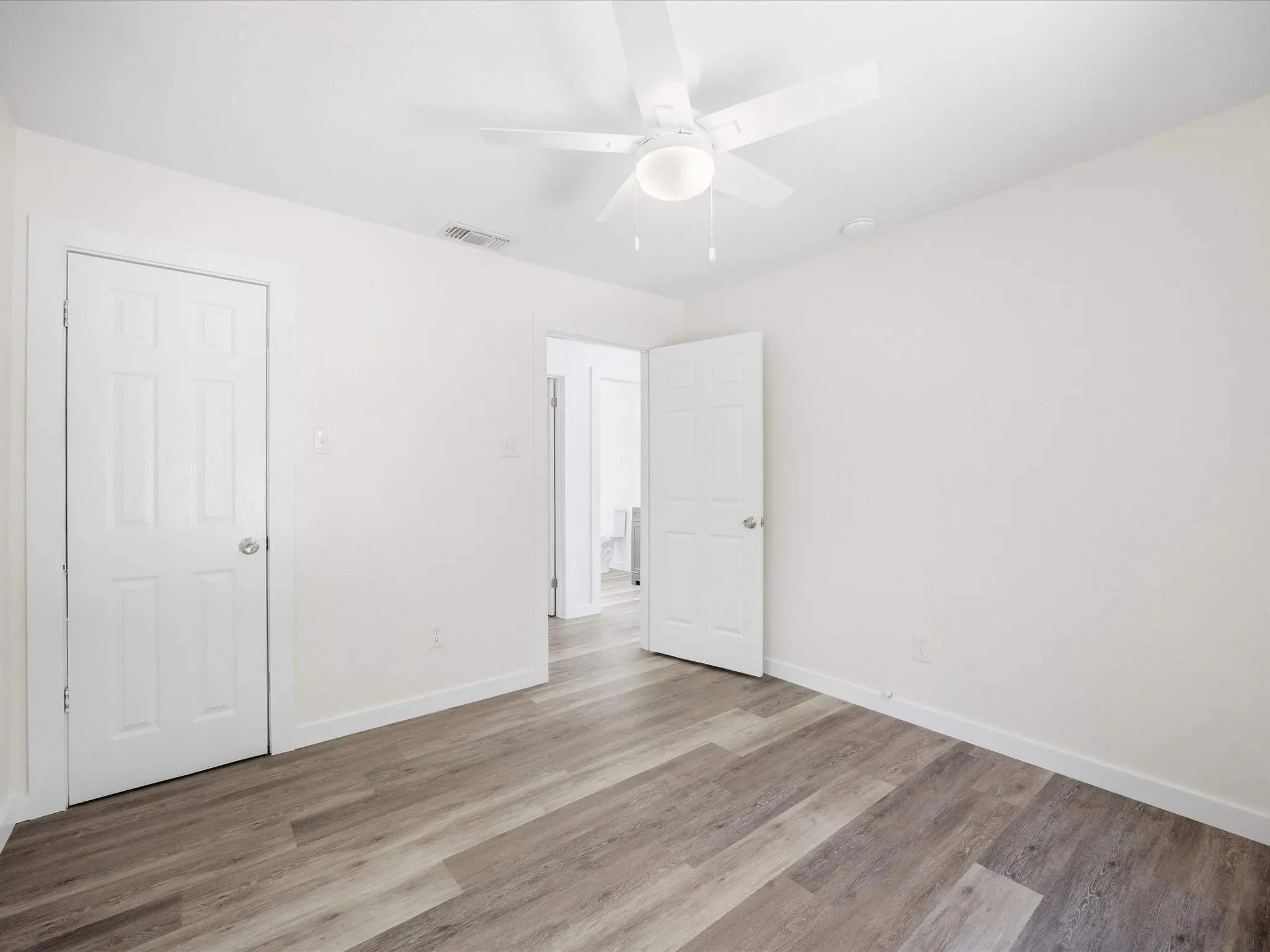 Wood-finish flooring, white walls, white ceiling fan with integrated lighting, and white paneled doors