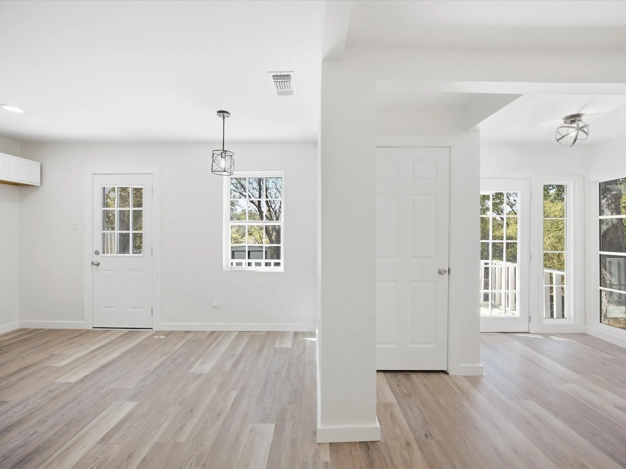 Wood-finish flooring, white paneled doors, multiple windows, recessed lighting, and a contemporary pendant light fixture