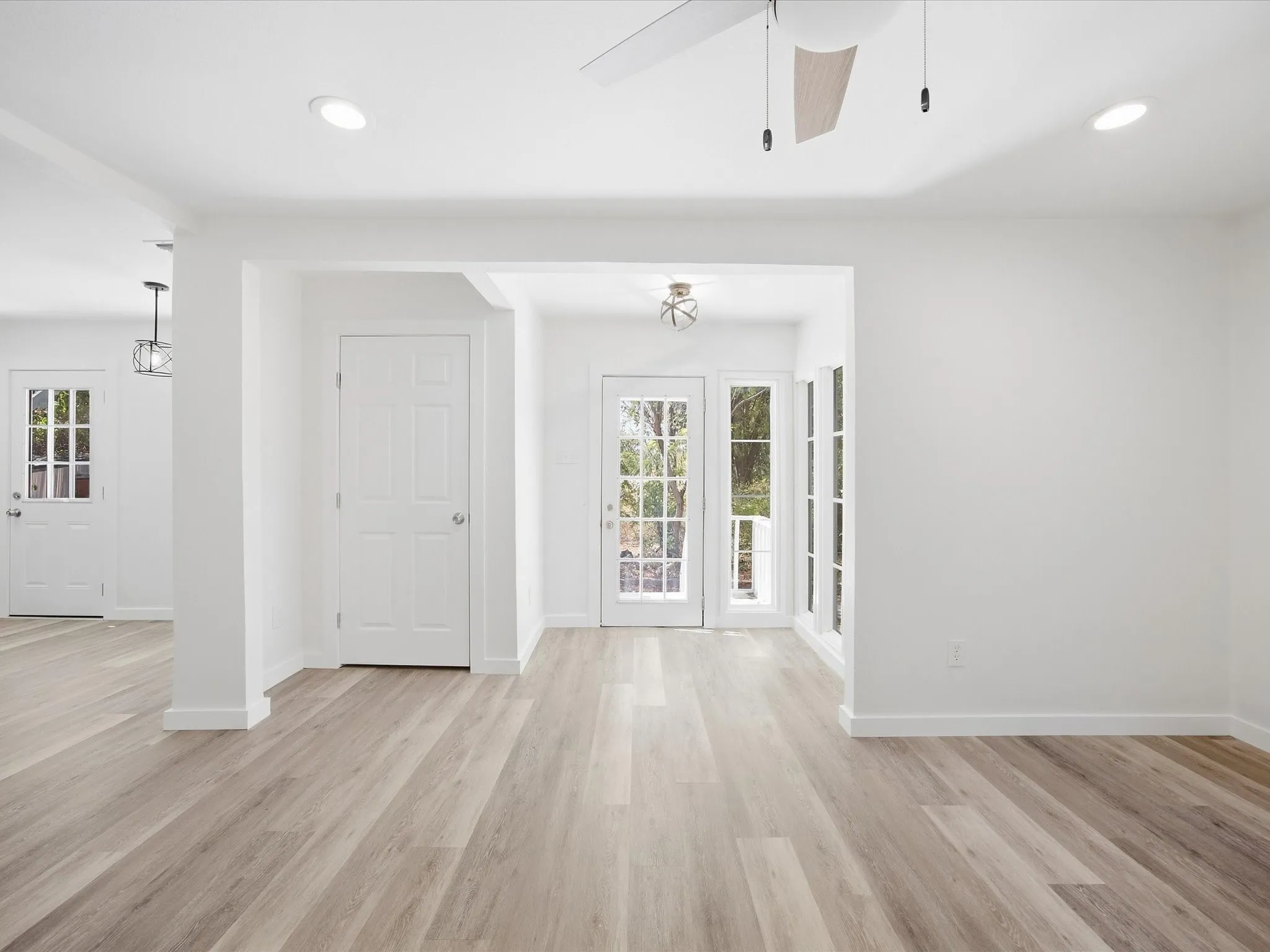 Wood-finish flooring throughout, recessed ceiling lighting, a ceiling fan with light, white paneled doors, and French doors with multiple window panes