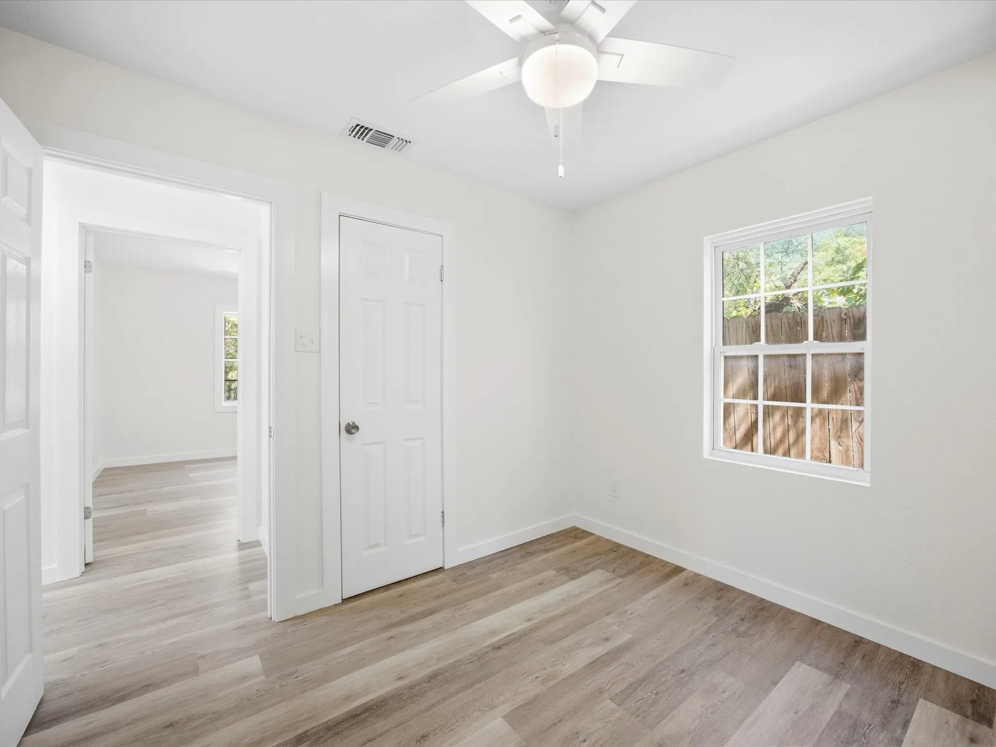 Wood-finish flooring throughout, bright white walls, and a ceiling fan with integrated lighting