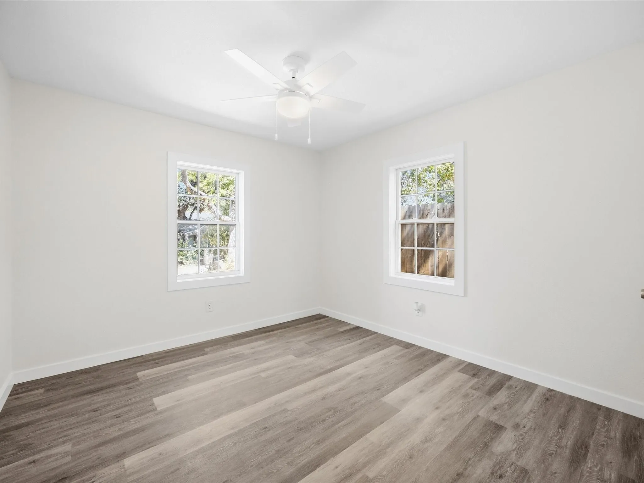 White walls, wood-finish flooring, two windows, and a ceiling fan with light fixture