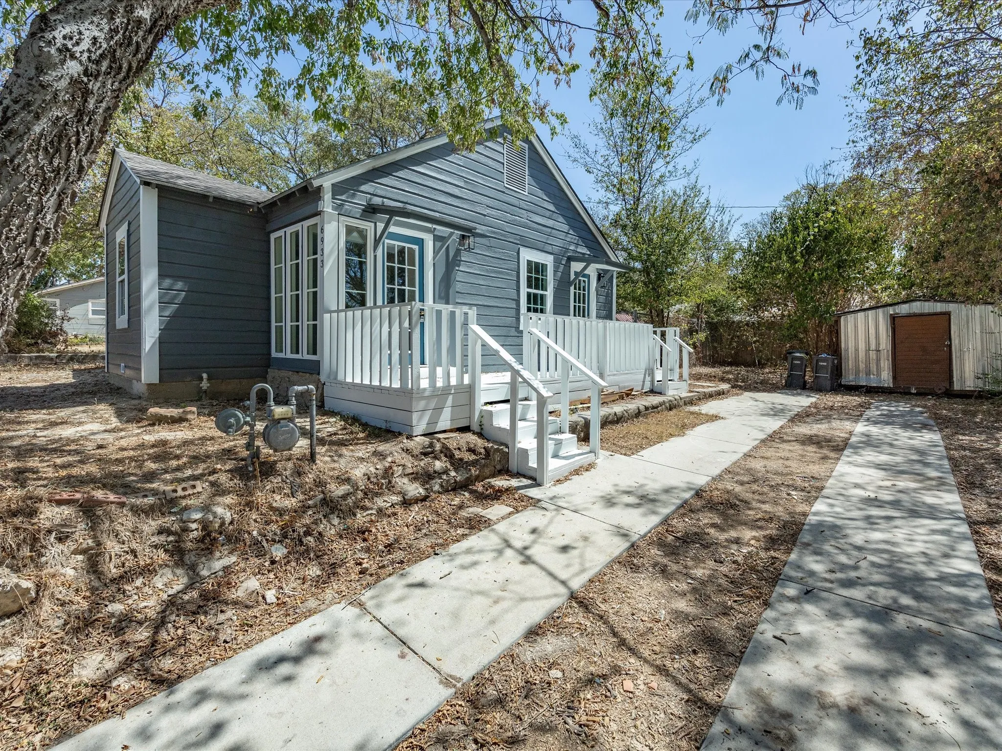 Exterior featuring blue siding, white window trim, a white porch with steps, and an adjacent concrete driveway