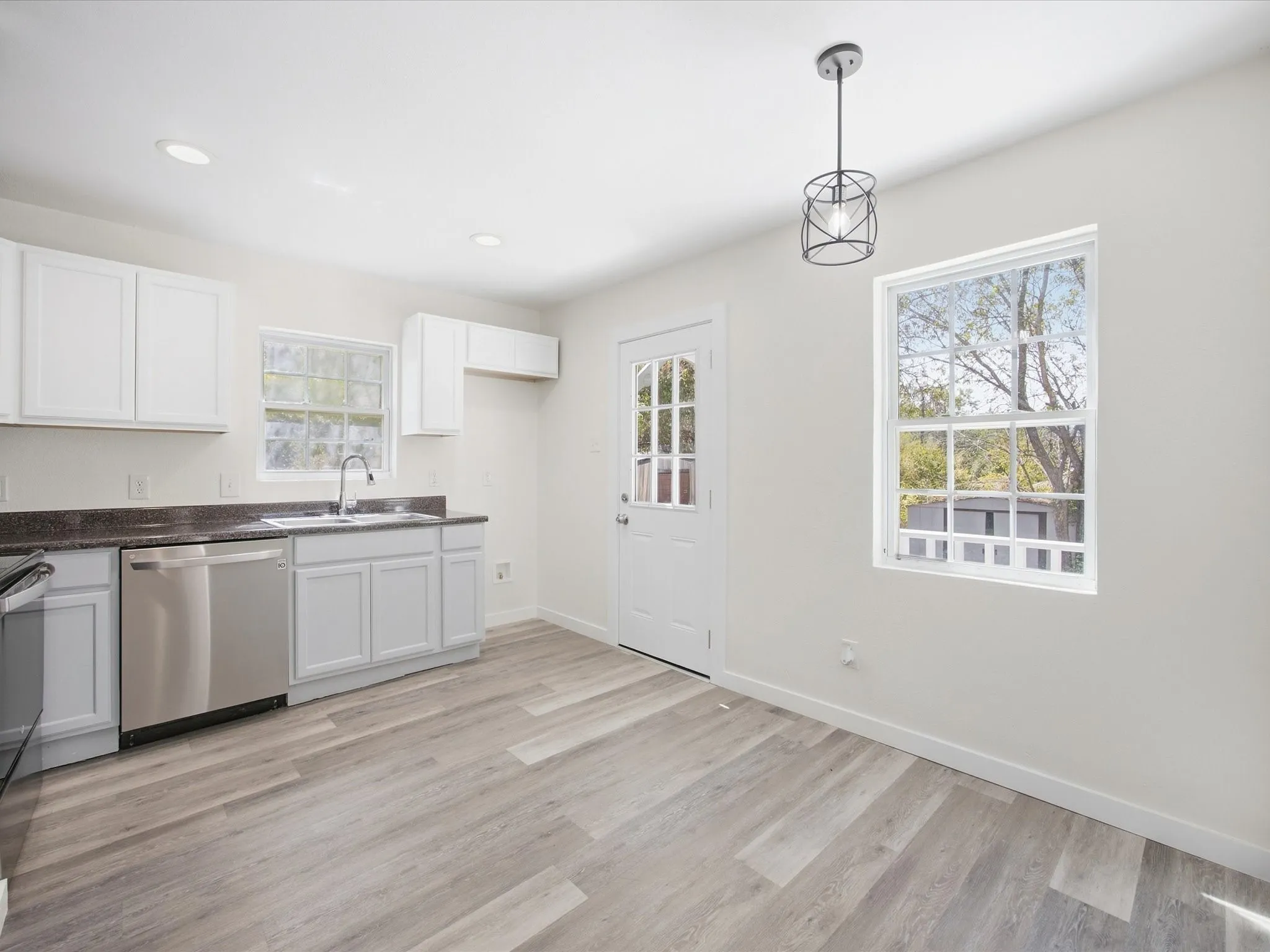 Kitchen featuring wood-finish flooring, white cabinetry, dark countertops, and stainless steel appliances
