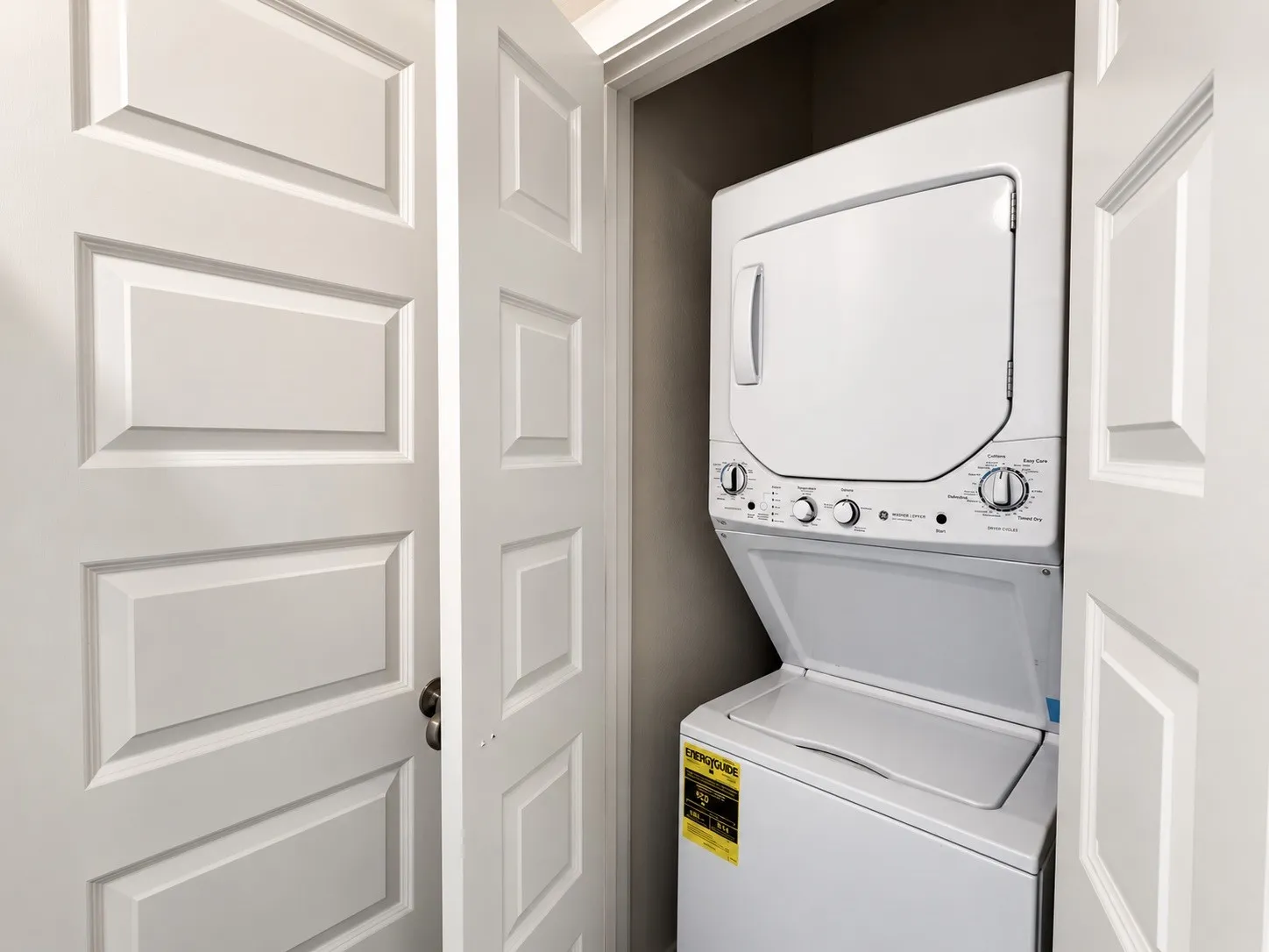 White stacked washer and dryer unit within a built-in closet, framed by paneled doors
