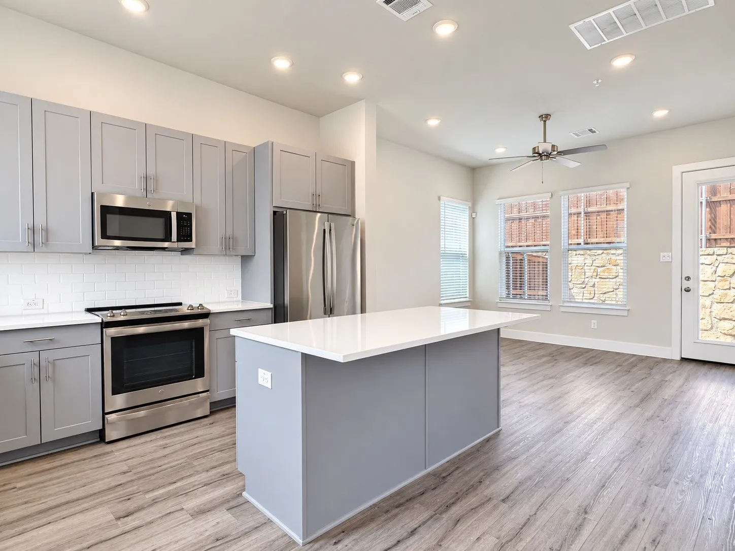 Kitchen featuring stainless steel appliances, a center island with a white countertop, subway tile backsplash, and wood-finish flooring