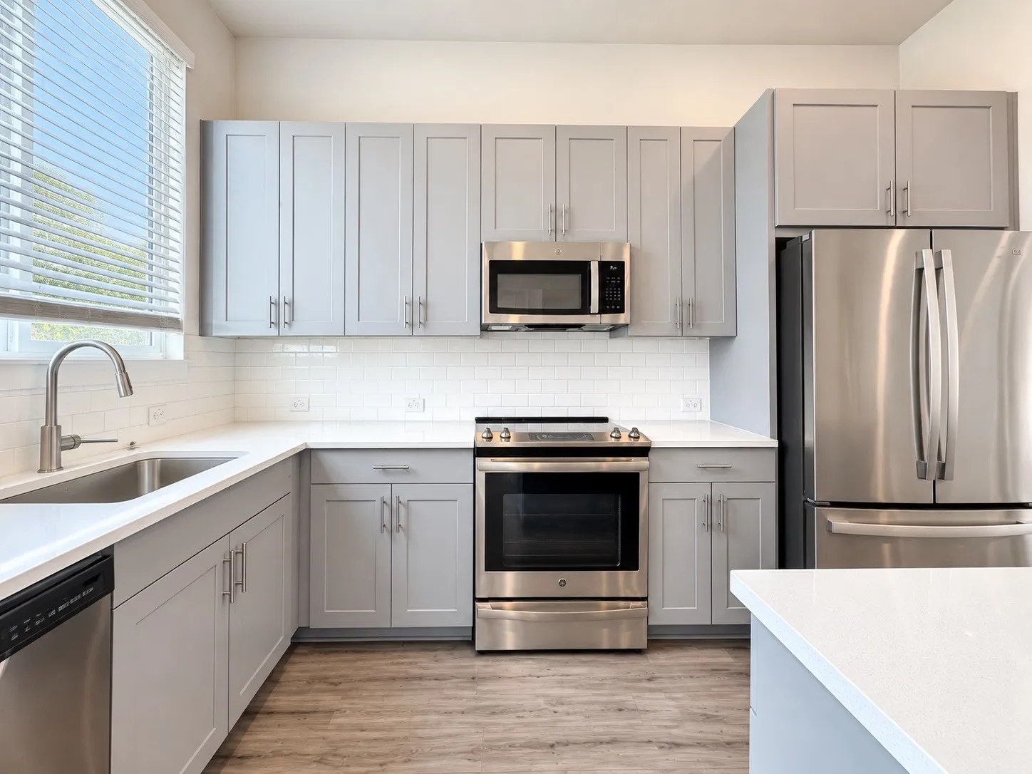 Kitchen featuring stainless steel appliances, white subway tile backsplash, light grey cabinetry, light-toned countertops, and wood-finish flooring