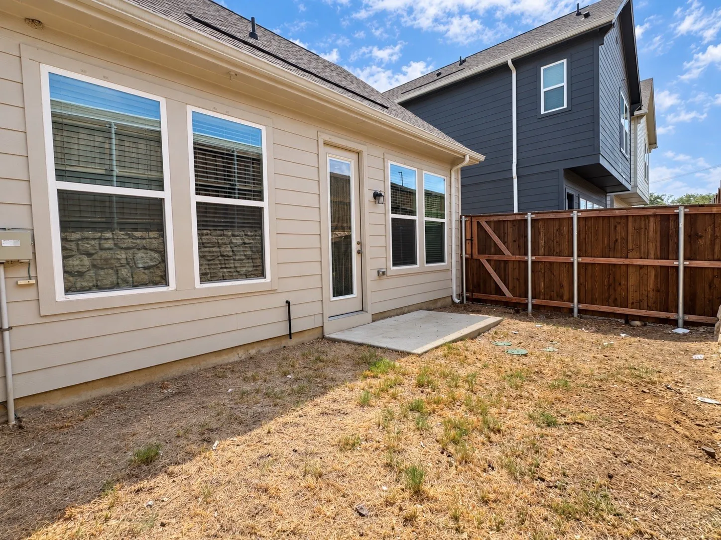 Rear exterior featuring a concrete patio, wood privacy fencing, and multiple windows
