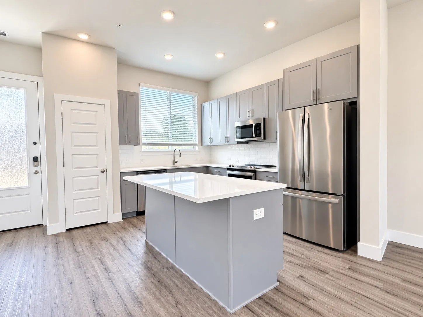 Kitchen featuring a central island with a white countertop, stainless steel appliances, gray cabinetry, white subway tile backsplash, and wood-finish flooring