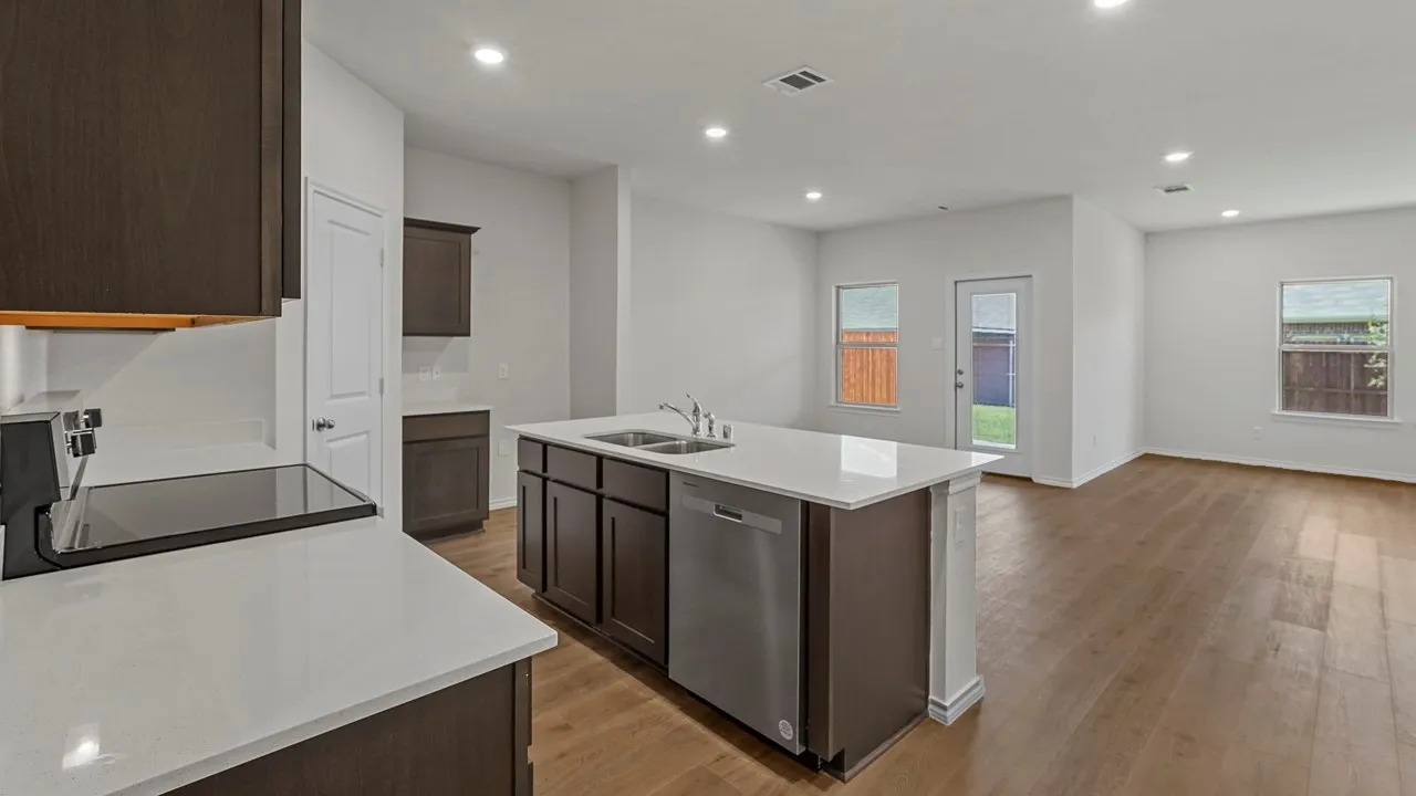 Kitchen featuring an island with a built-in sink and dishwasher, white countertops, dark wood-finish cabinetry, a ceramic cooktop, and recessed lighting