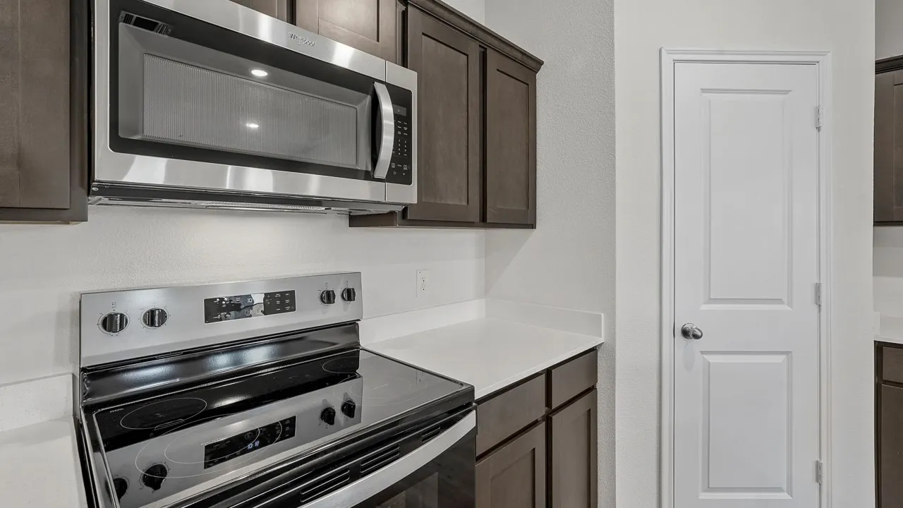 Stainless steel microwave, electric range, dark wood-finish cabinetry, and white countertops