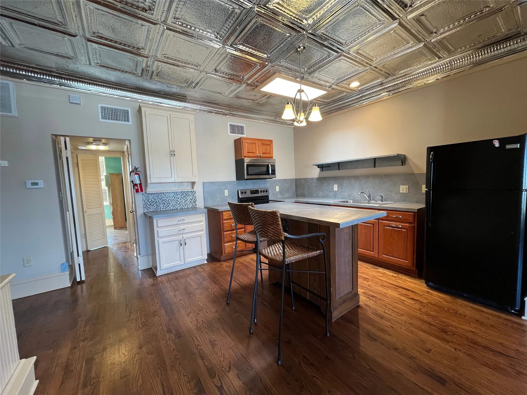 Hardwood flooring, pressed tin ceiling, kitchen island with countertop, built-in cabinetry, and integrated appliances
