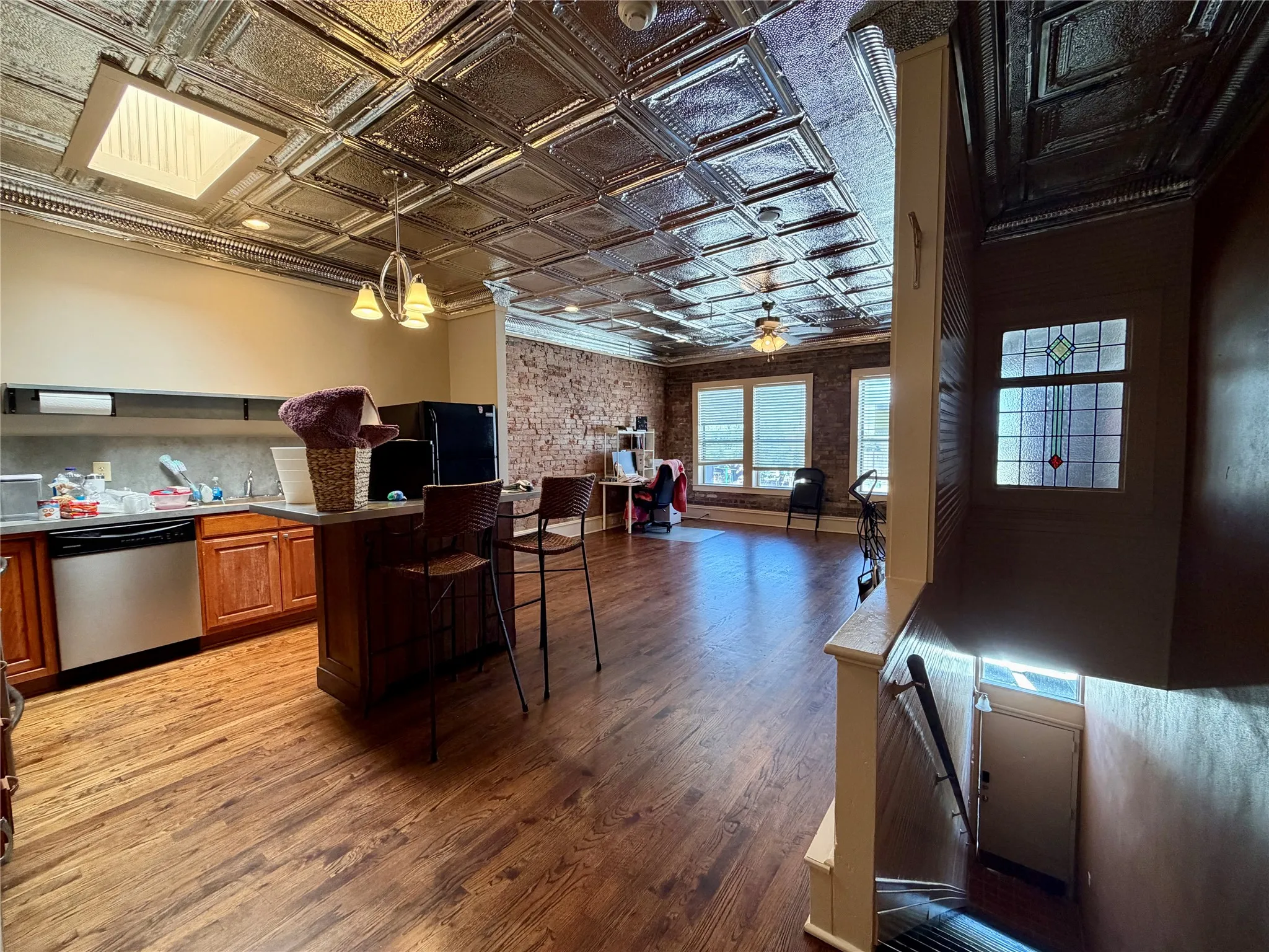 Wood-finish flooring throughout, pressed tin ceiling with recessed lighting, exposed brick wall detail, and a built-in kitchen island with counter seating