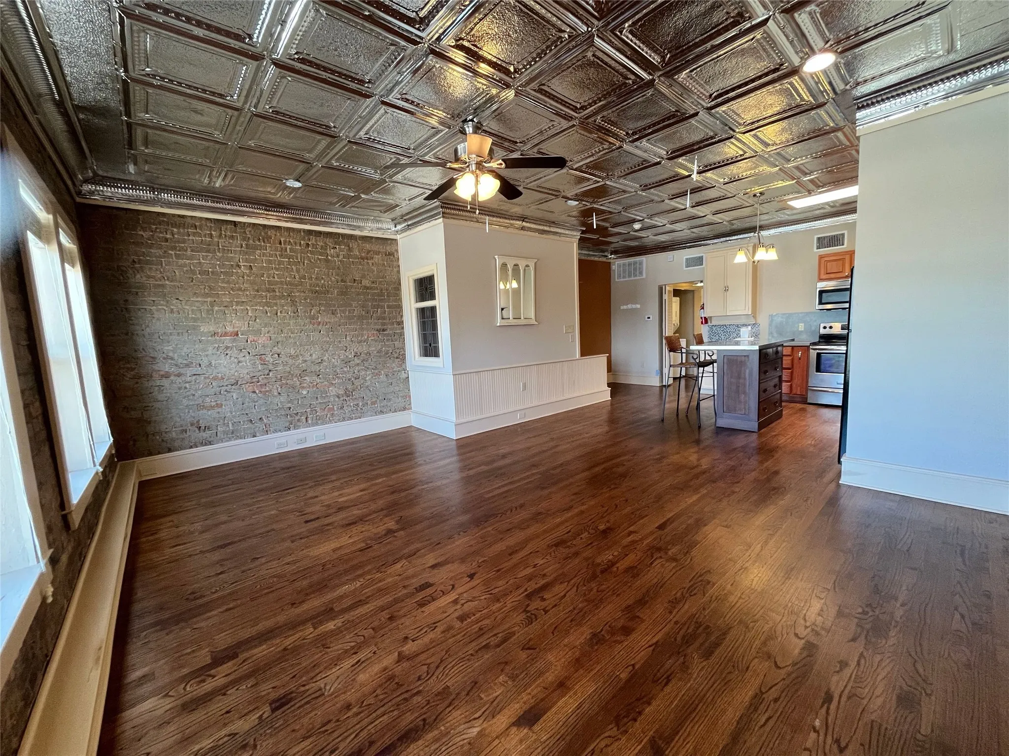 Hardwood flooring, exposed brick wall, tin ceiling, ceiling fan, and stainless steel appliances
