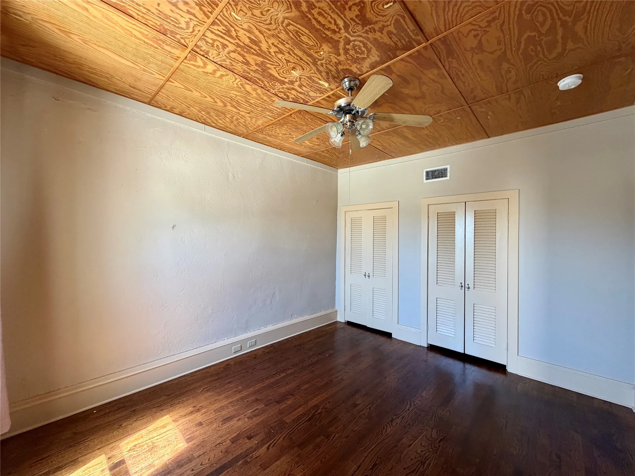 Wood-finish flooring, paneled ceiling, two sets of louvered closet doors, and ceiling fan with integrated lighting