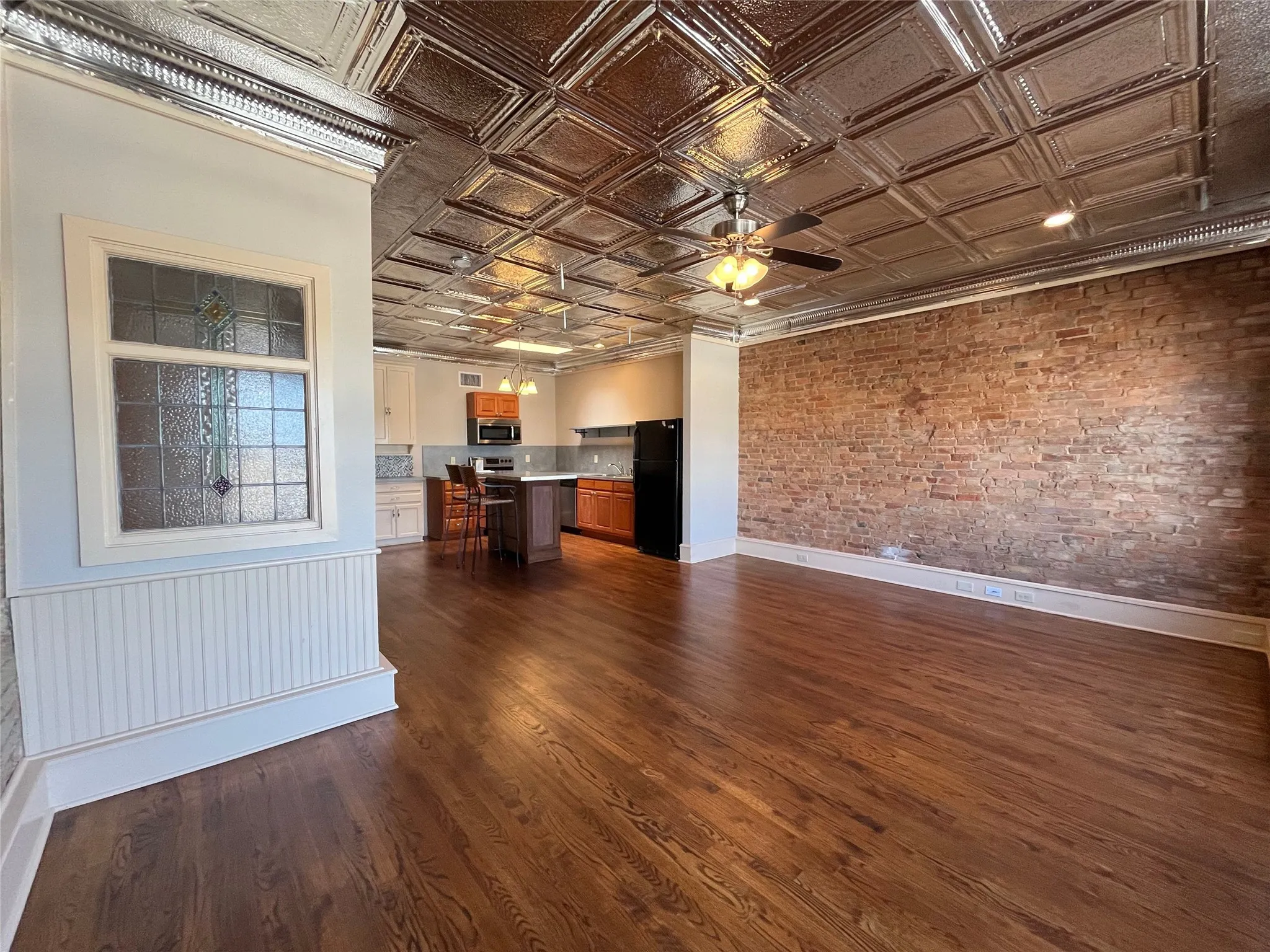 Hardwood flooring, exposed brick accent wall, decorative tin ceiling, wainscoting, and an open-concept kitchen with island seating