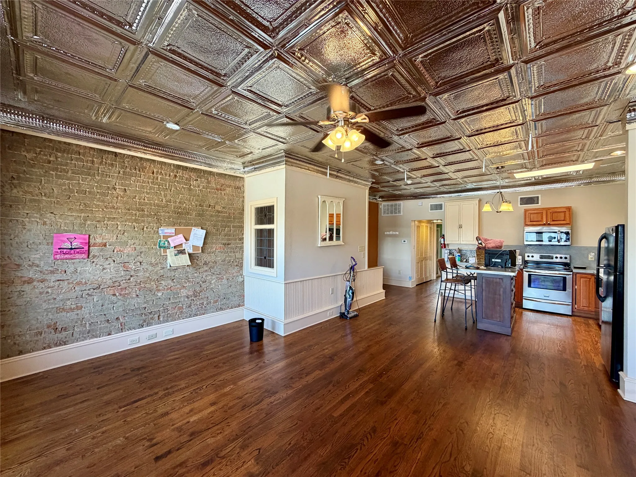 Pressed tin ceiling, exposed brick wall, wood-finish flooring, kitchen island, and stainless steel appliances
