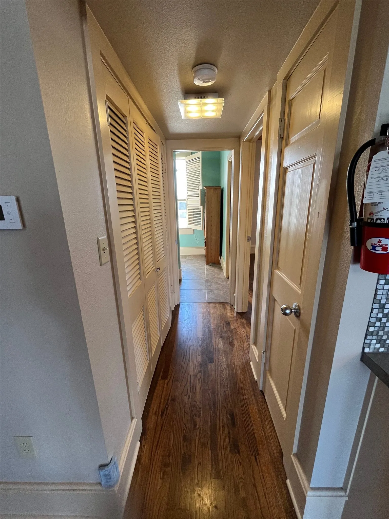 Hallway featuring wood-finish flooring, louvered bi-fold doors, and recessed panel doors