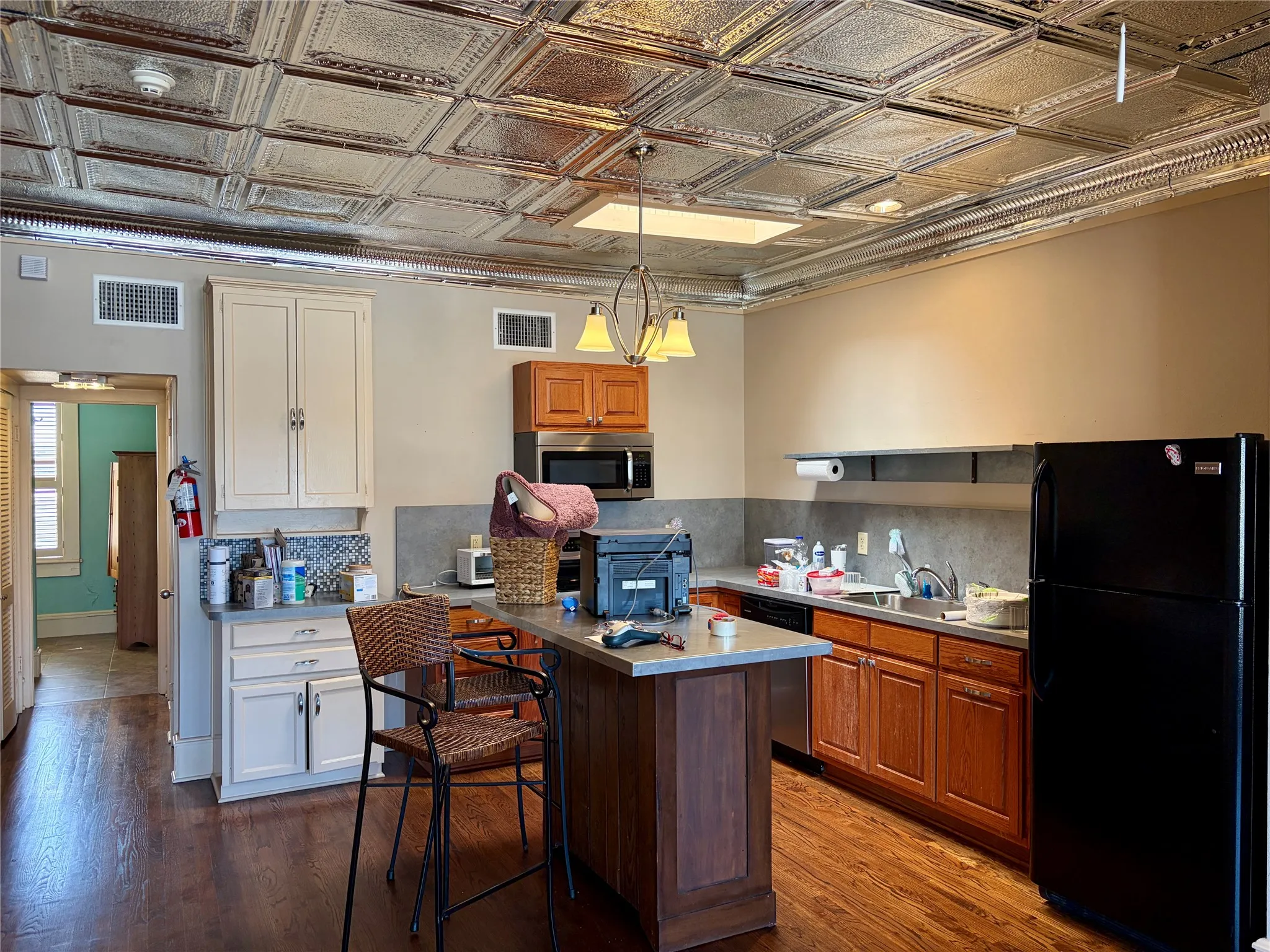 Pressed tin ceiling, wood-finish flooring, two-tone cabinetry, stainless steel appliances, and a central island with countertop seating