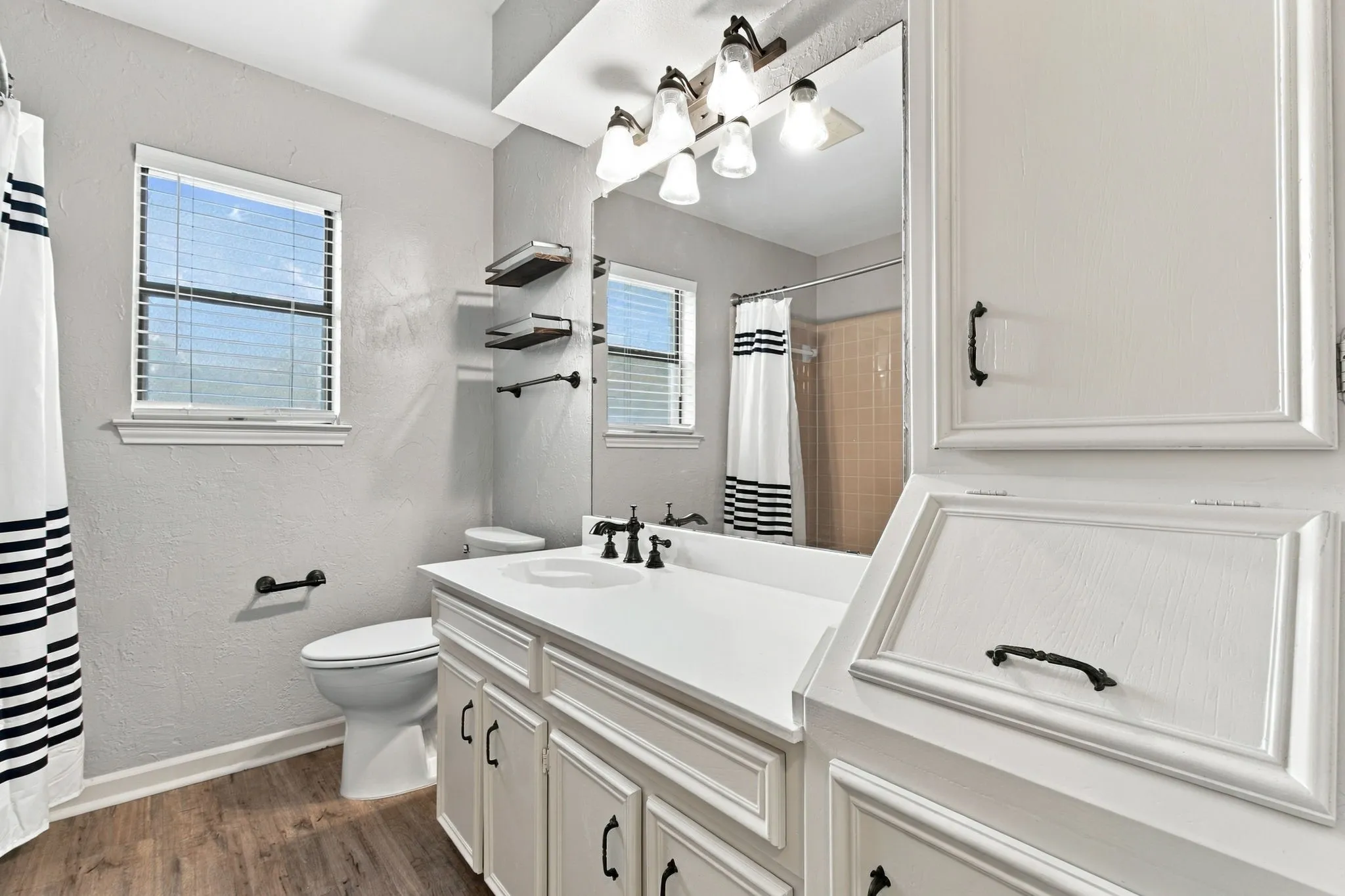 White vanity with an integrated sink, black fixtures, and wood-finish flooring