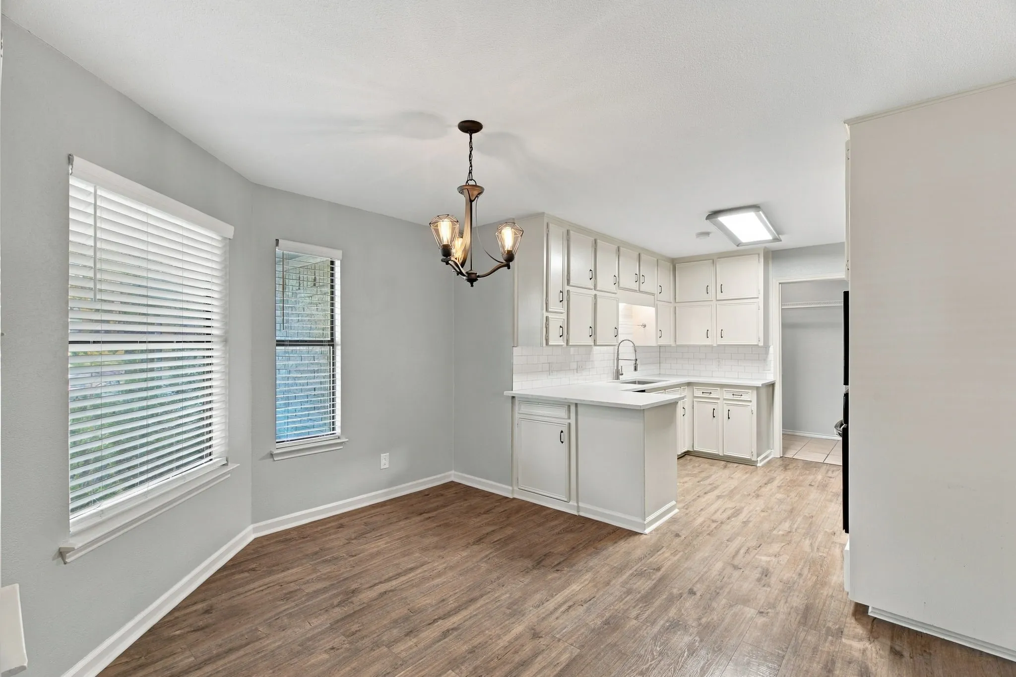 Open-concept living area with wood-finish flooring, a contemporary chandelier, and a kitchen featuring white cabinetry, a white subway tile backsplash, and a white countertop
