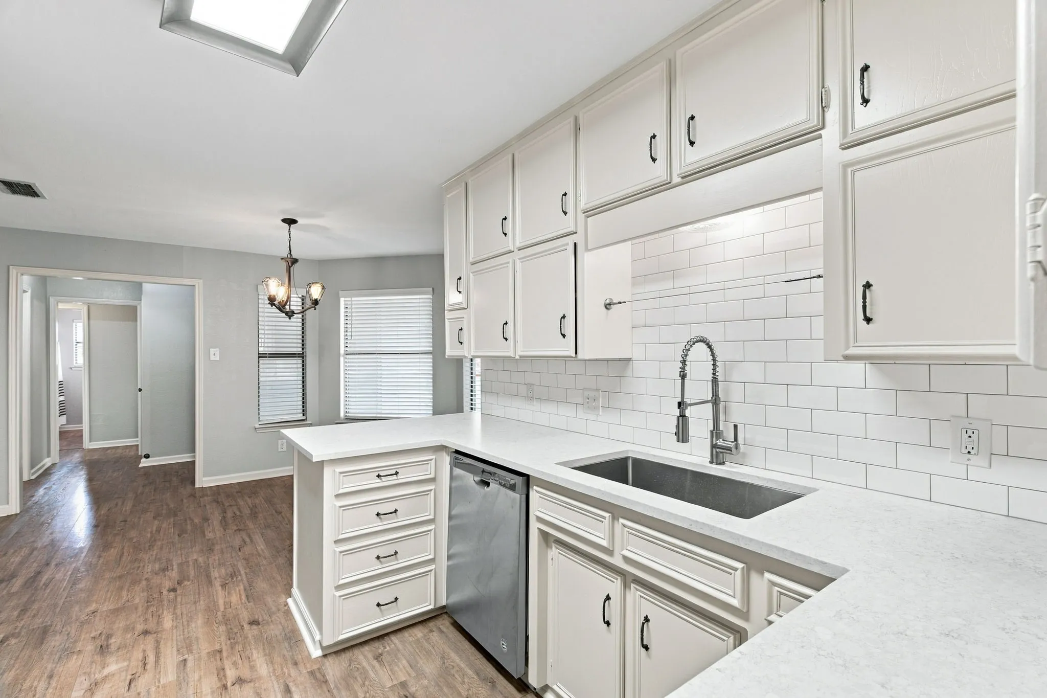 White cabinetry, light countertops, subway tile backsplash, stainless steel sink with gooseneck faucet, and wood-finish flooring