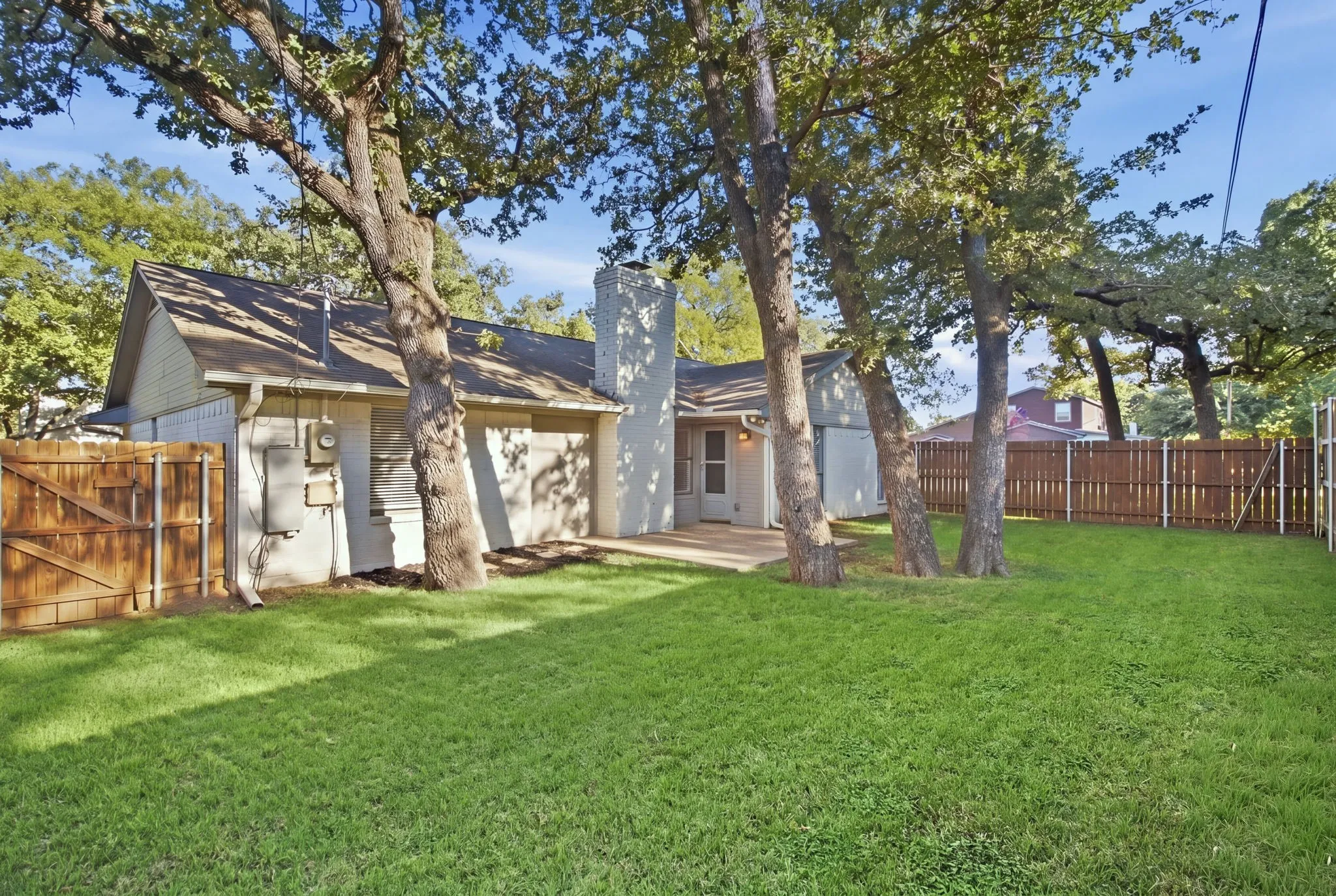 Expansive backyard featuring a manicured lawn, mature trees, a wood privacy fence, and a patio area