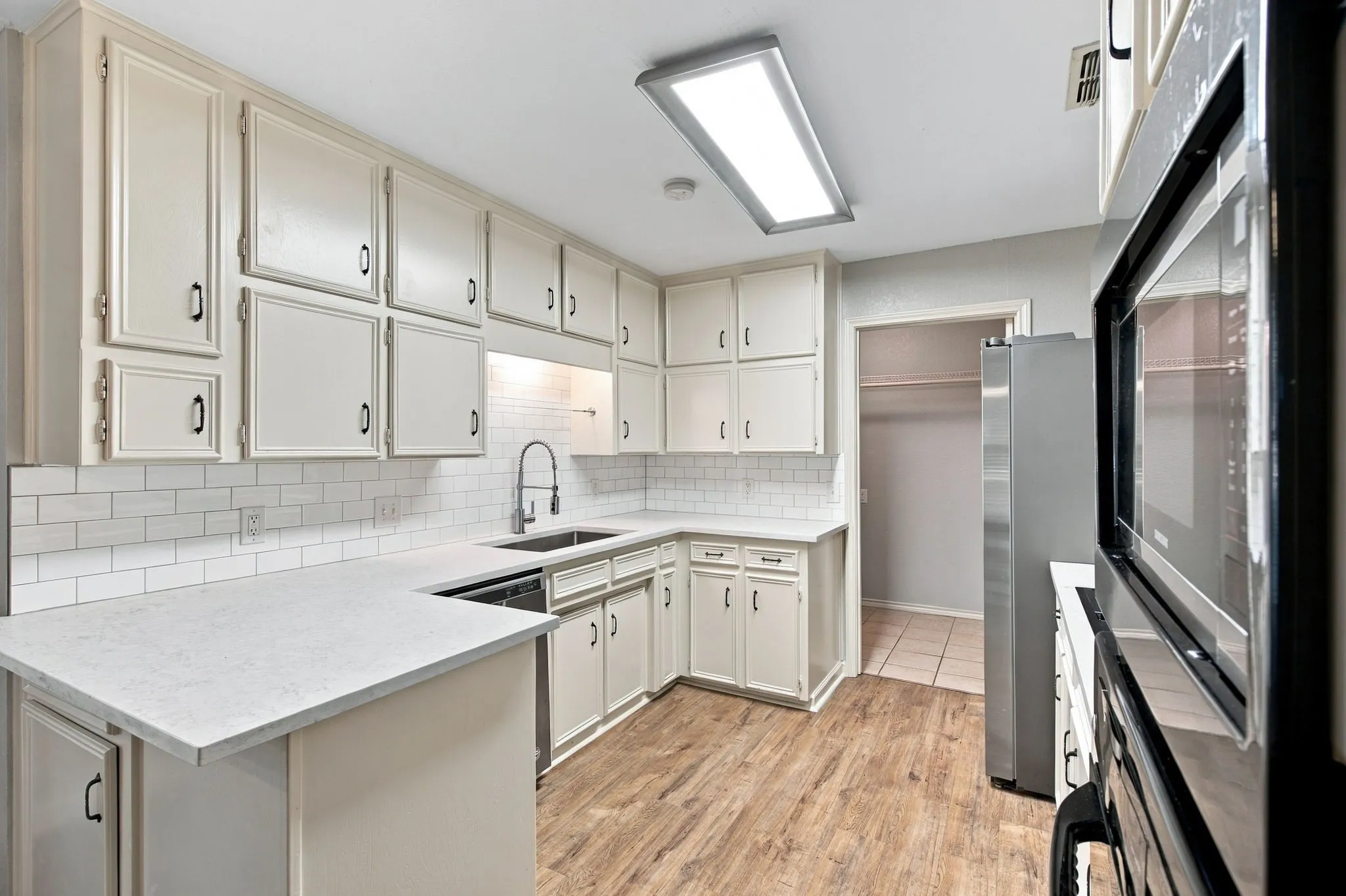 Kitchen featuring extensive light-toned cabinetry, subway tile backsplash, white countertops, wood-finish flooring, and built-in stainless steel appliances