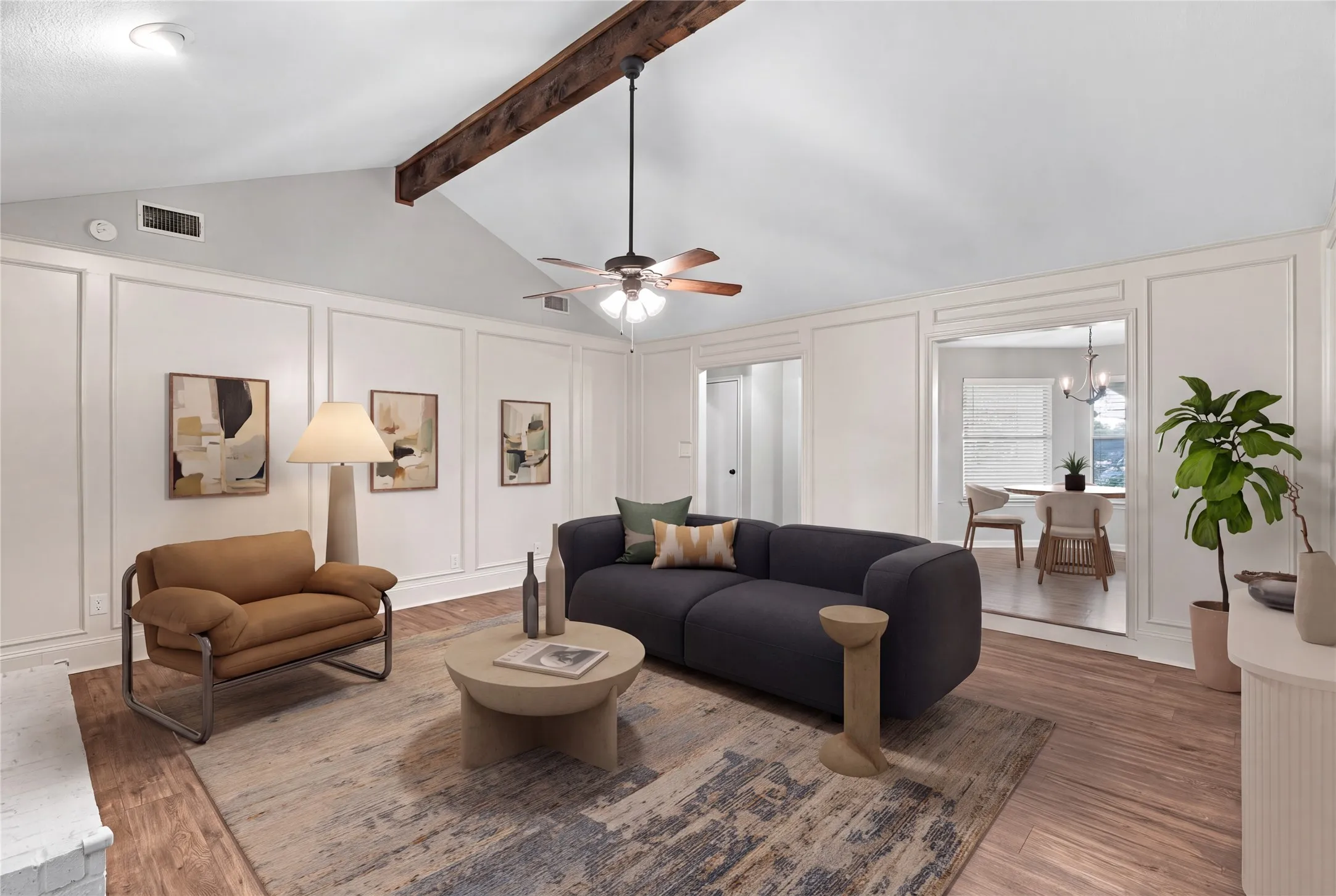 Vaulted ceiling with exposed beam, wood-finish flooring, decorative wall molding, ceiling fan with light fixture (Virtually staged)