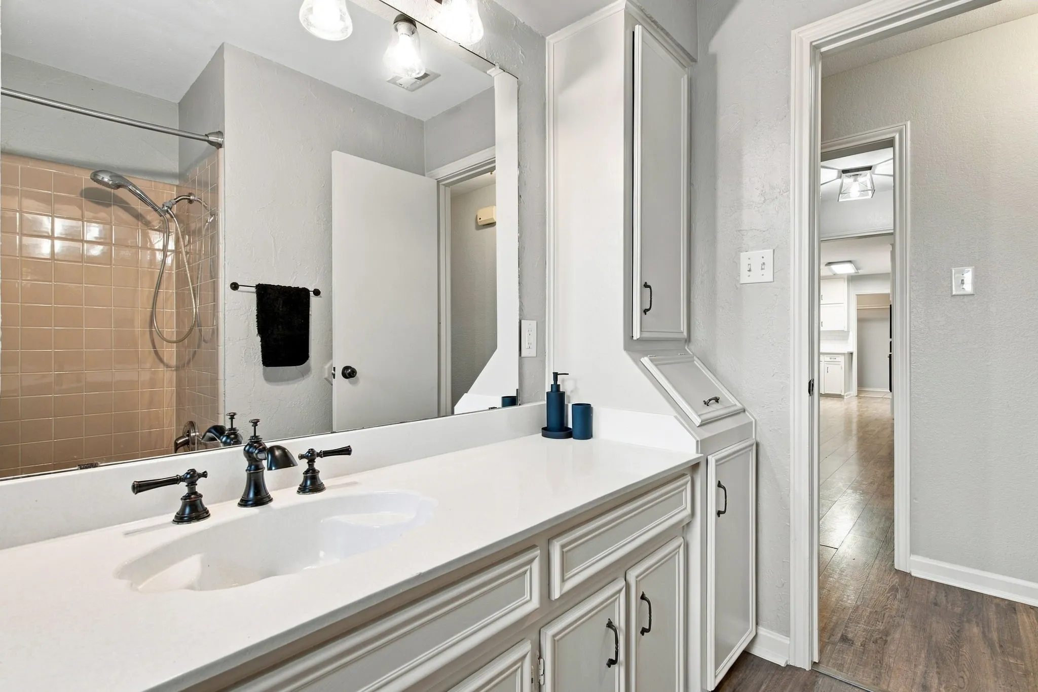Bathroom featuring a shower with tan tile surround, white vanity with integrated sink, black-finish faucet, and built-in storage cabinetry