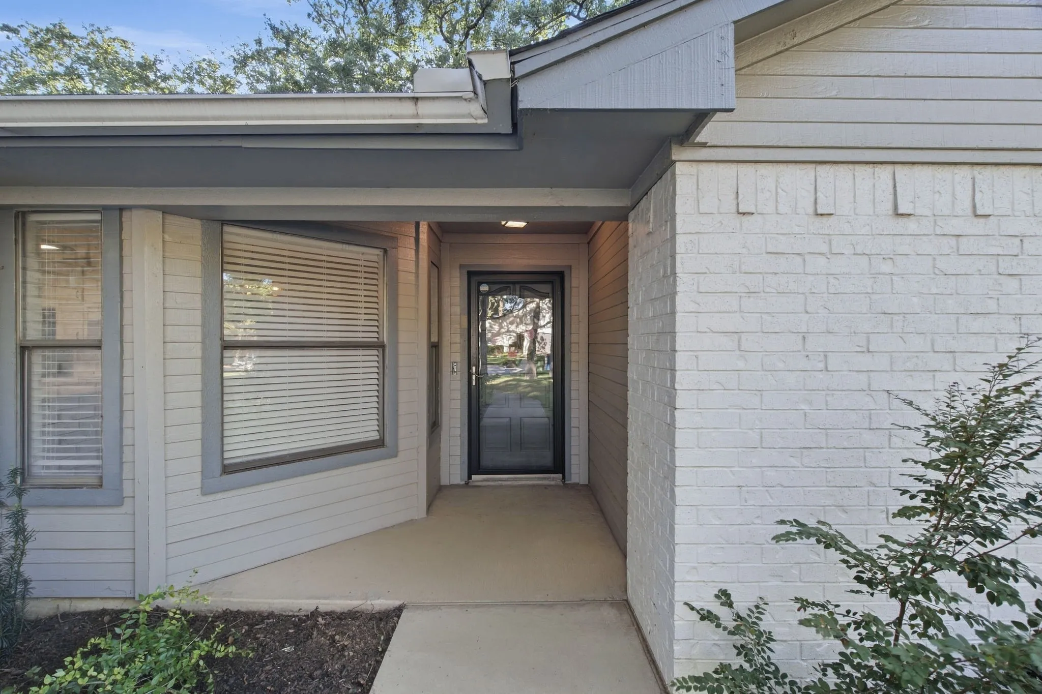 Entryway featuring a security screen door, an overhang, and mixed siding with brick and horizontal panels