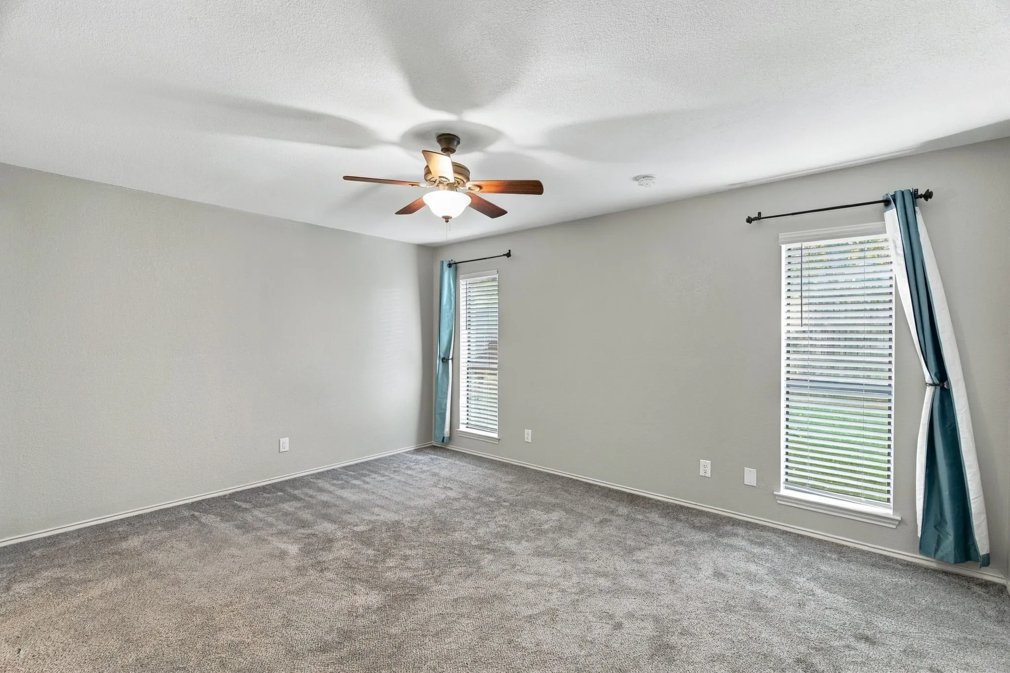 Spacious room with plush gray carpeting, neutral wall paint, and a ceiling fan with integrated lighting