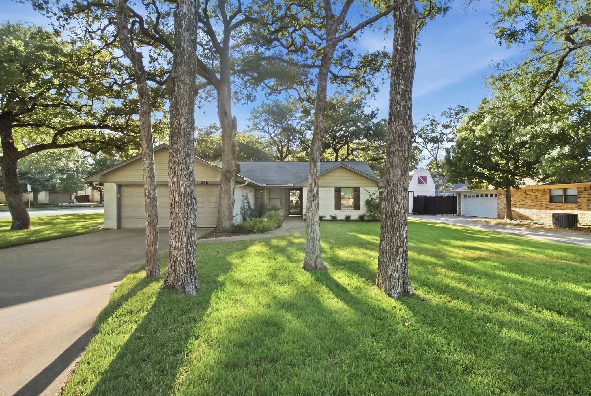 Expansive front lawn with mature trees, a paved driveway, and a two-car garage